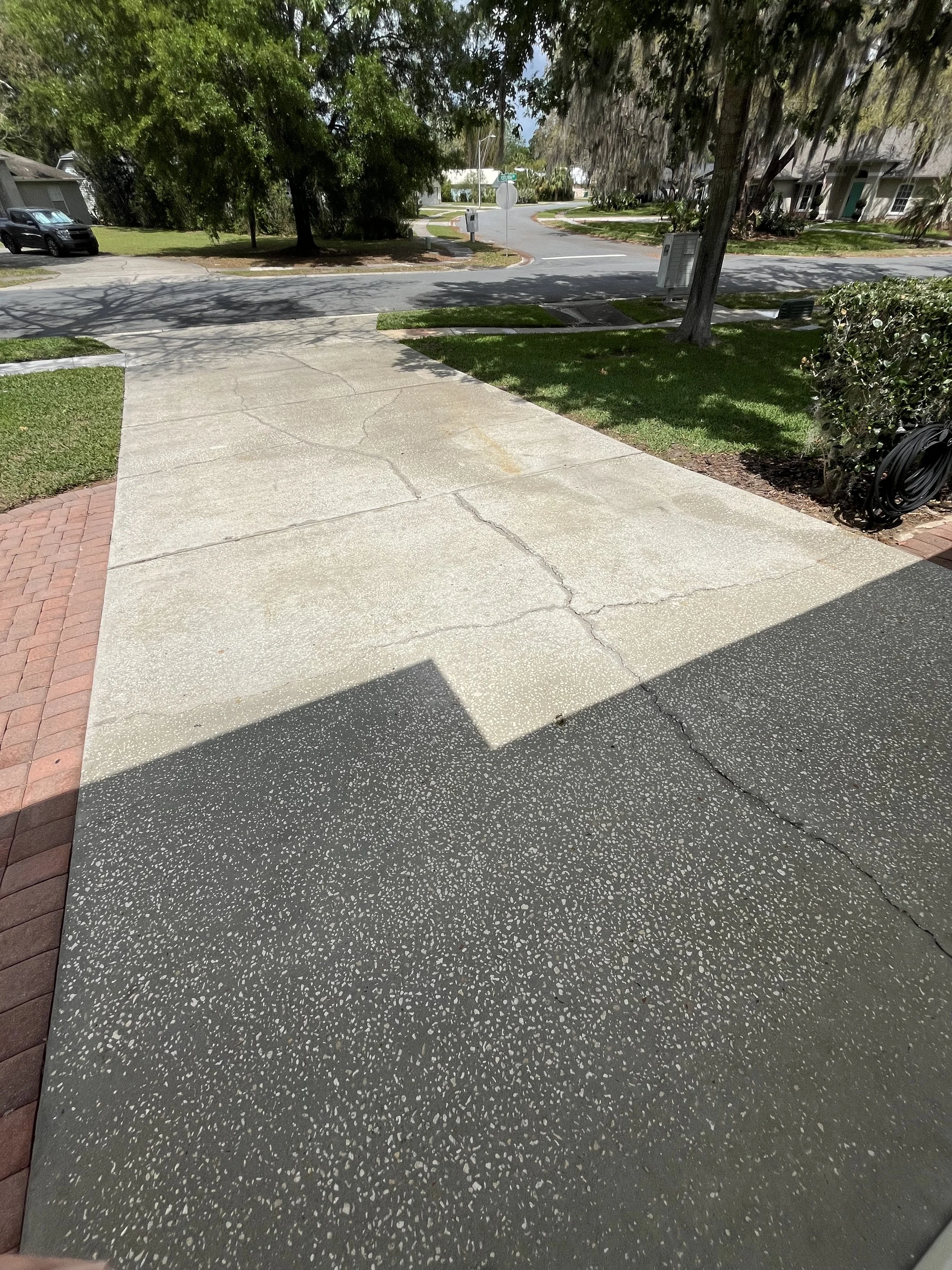 View of a residential street from a front porch with concrete and paver sidewalk, trees, grass, and houses in the background.