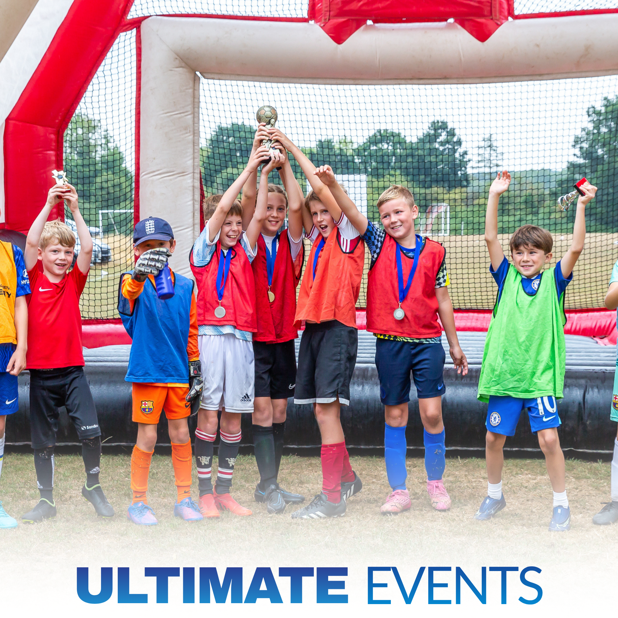 Group of children celebrating with medals and holding a trophy in front of a goal net on a field.