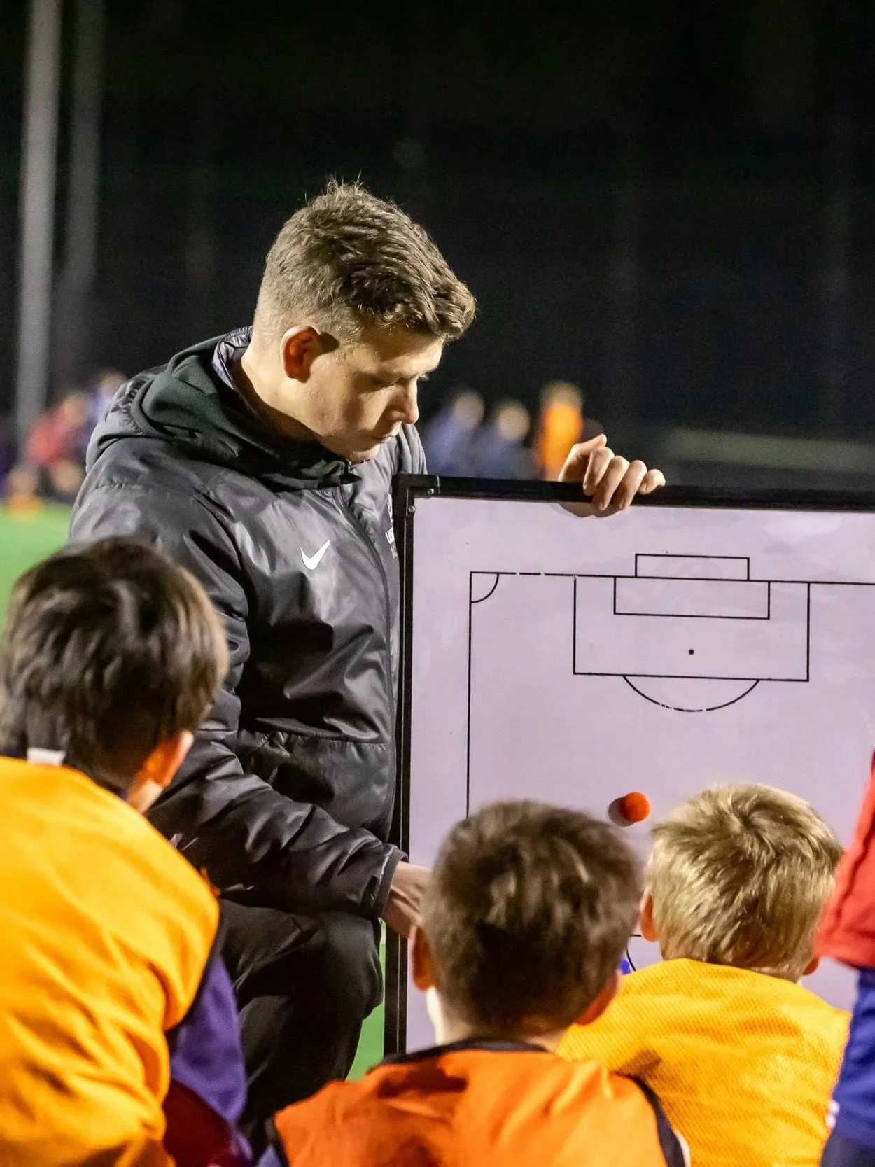 A coach shows a tactical diagram on a whiteboard to young soccer players during a practice session.