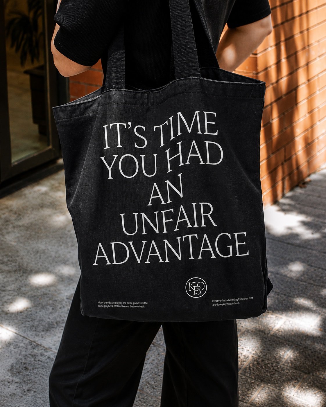 Person holding a black tote bag (KBO MARKETING Merch) "IT'S TIME YOU HAD AN UNFAIR ADVANTAGE." -