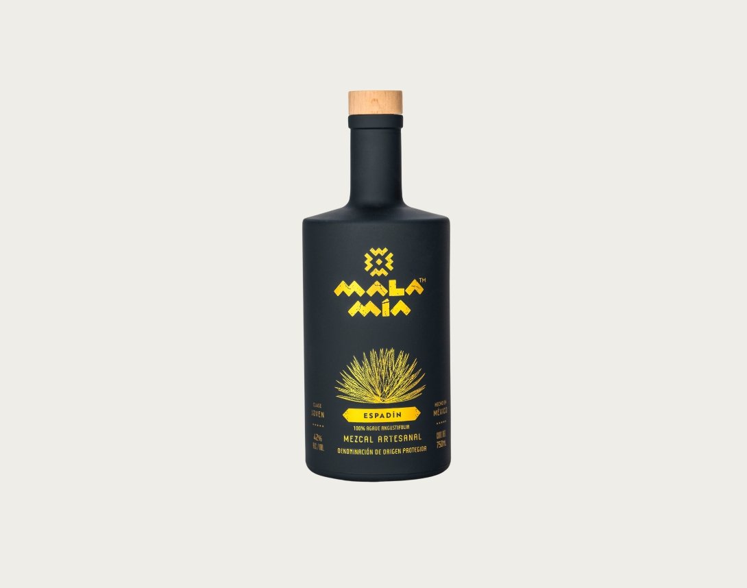 A black bottle of Mala Mía espadin mezcal with a wooden cap and yellow label featuring a graphic of an agave plant and text saying 100% agave.