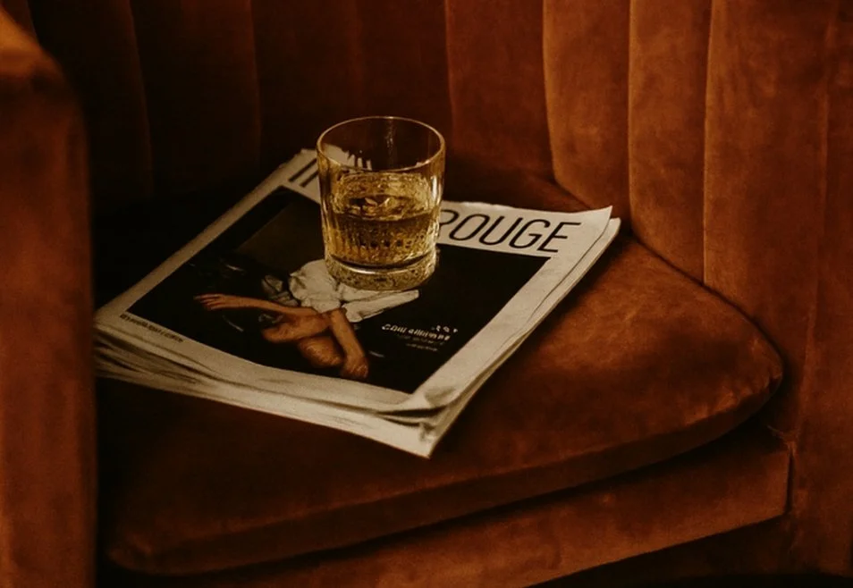 A glass of a mezcal drink or cocktail made with Mala Mía Mezcal, and a black and white magazine resting on a brown velvet chair.