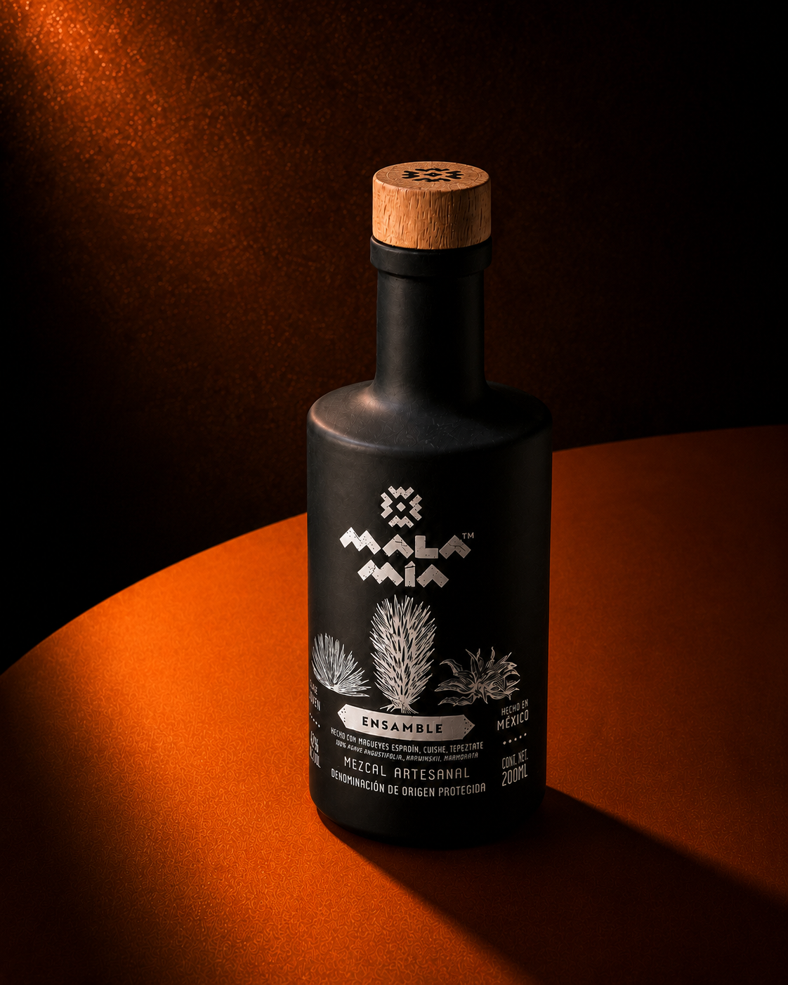 A black bottle of mala mia mezcal ensamble with a wooden cap, featuring illustrations of agave plants and text indicating it is an artisanal mezcal from Mexico.