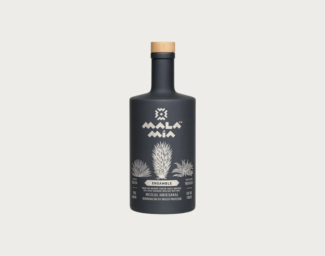 A black bottle of Malla Mia Ensamble mezcal with a wooden cap, featuring white illustrations of types of agave plants and white text.