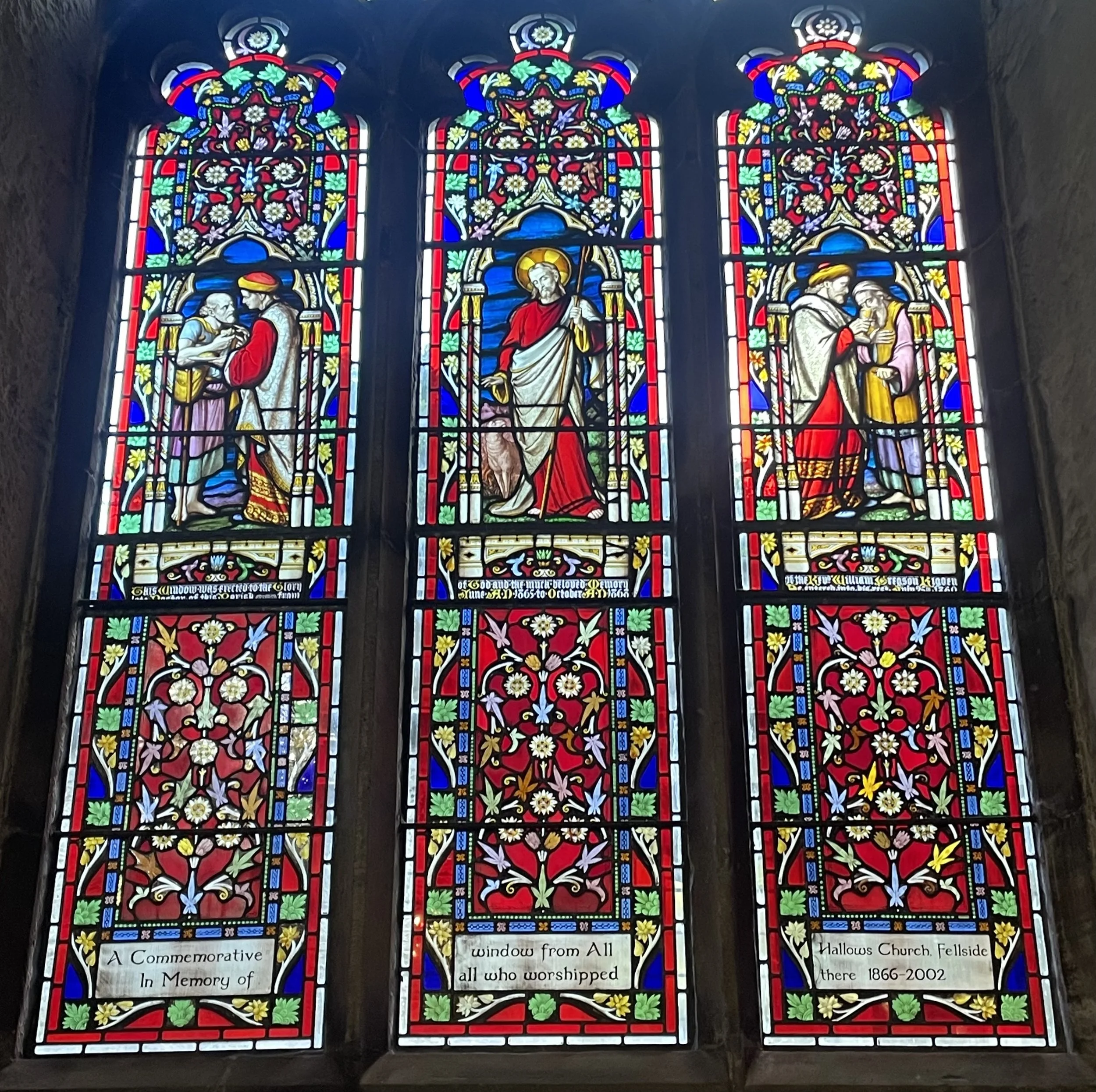 Colorful stained glass window with religious scenes and inscriptions, located in a church.