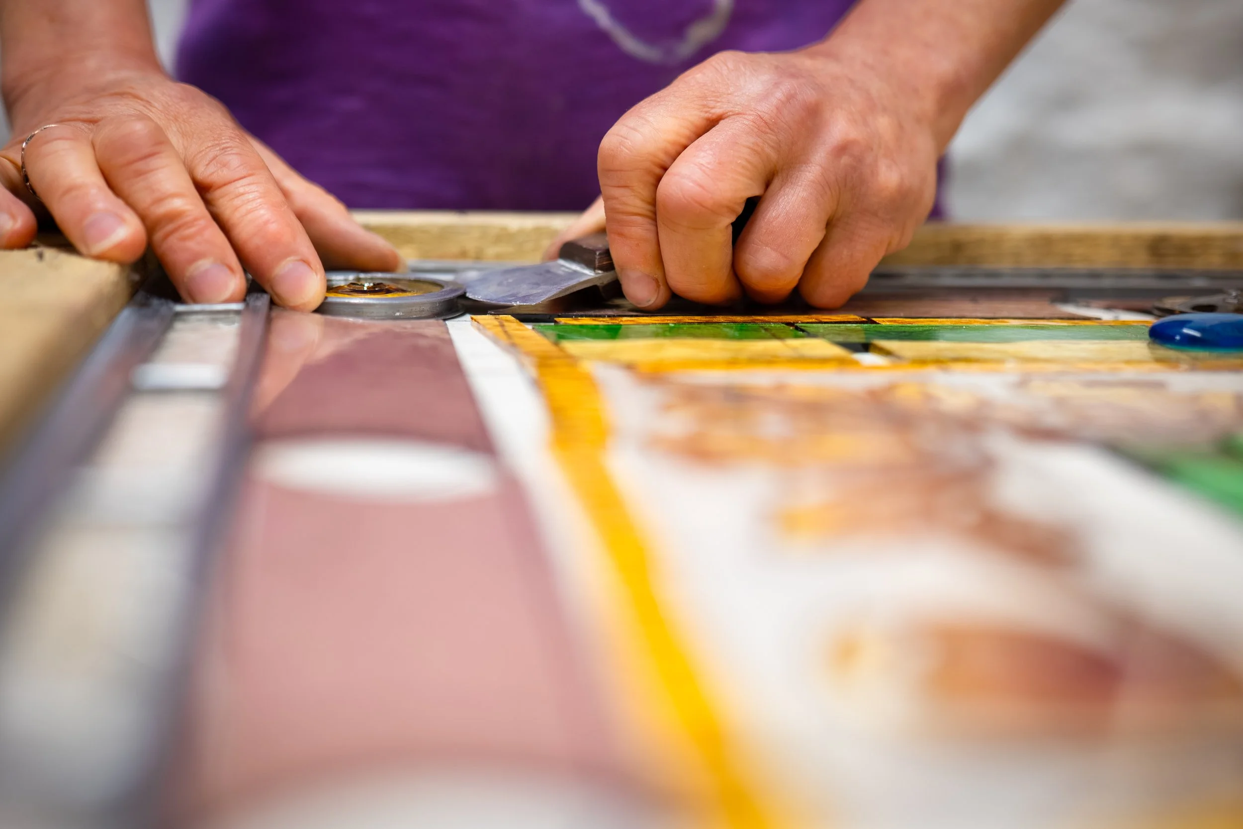 Close-up of a person's hands using a pizza cutter to cut a colorful pizza on a wooden surface.