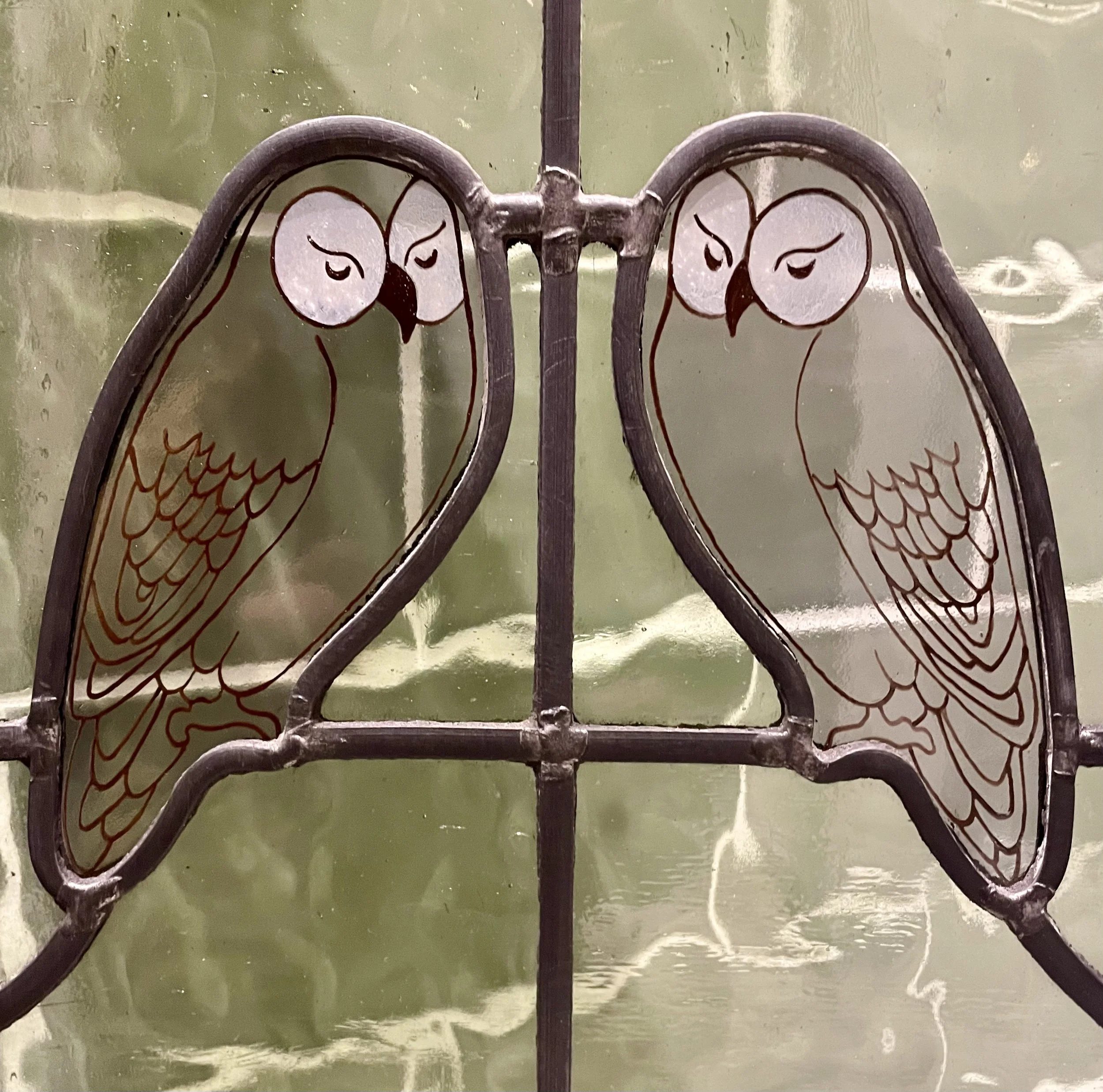 Close-up of stained glass window featuring two outlined dove figures with wings, set against a green background.