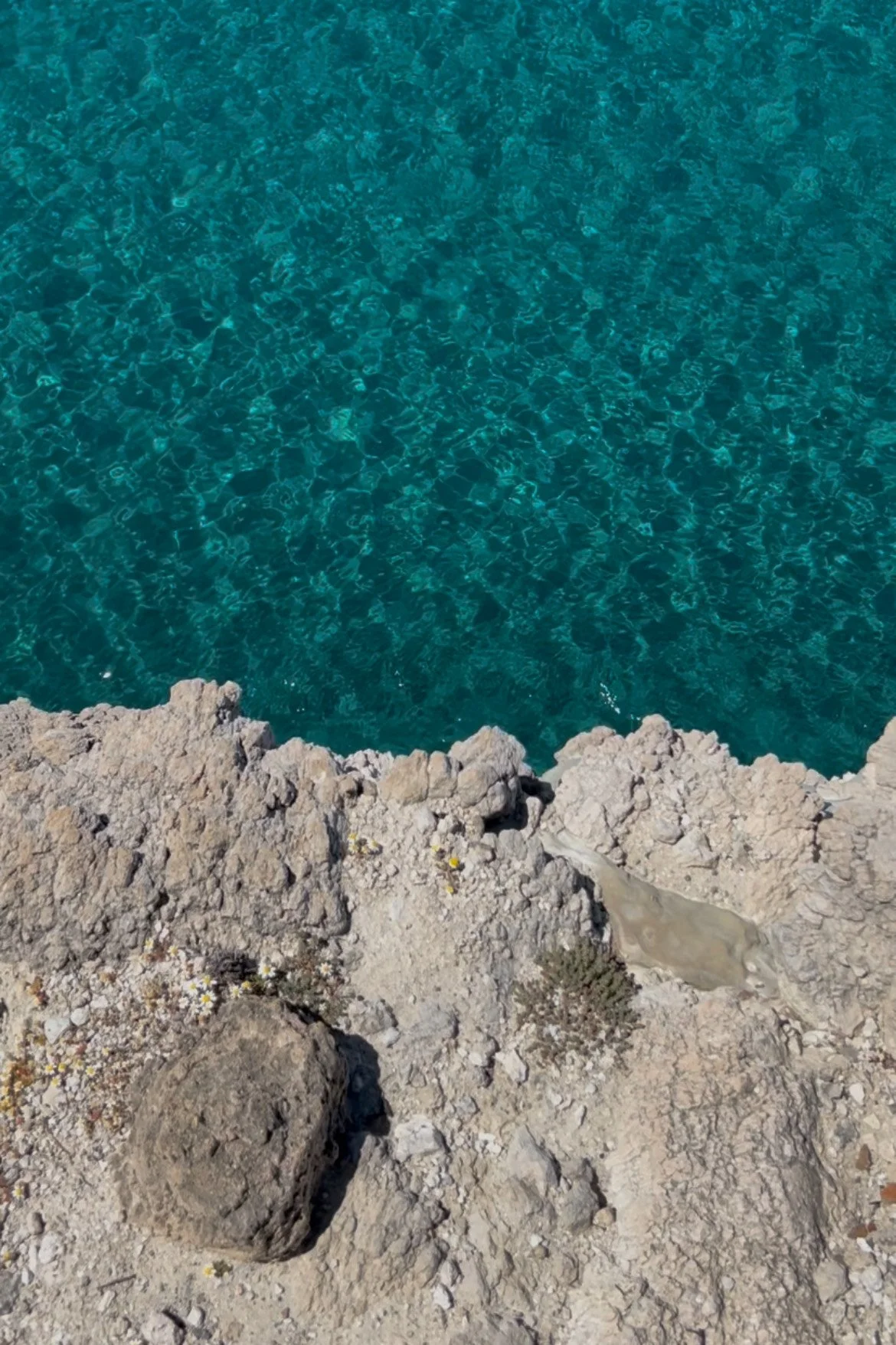 Cliffside view of blue ocean water with rocky shoreline in the foreground.