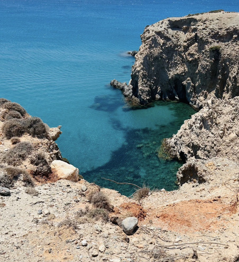 Cliff overlooking a deep blue ocean with rocky formations and sparse desert vegetation.