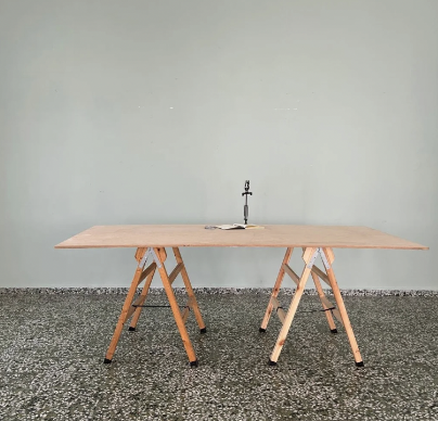 Empty wooden table with a candlestick and a book on it against a plain wall.