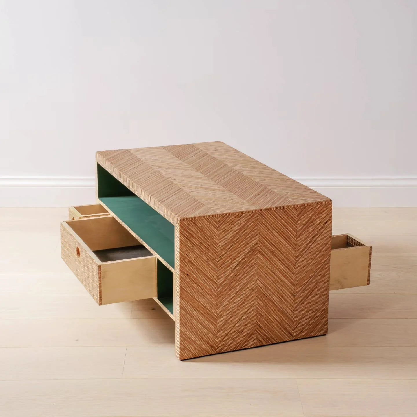 A modern wooden side table with multiple drawers, featuring a unit with natural wood finish, green interior, and a small drawer pull, placed against a plain white wall.