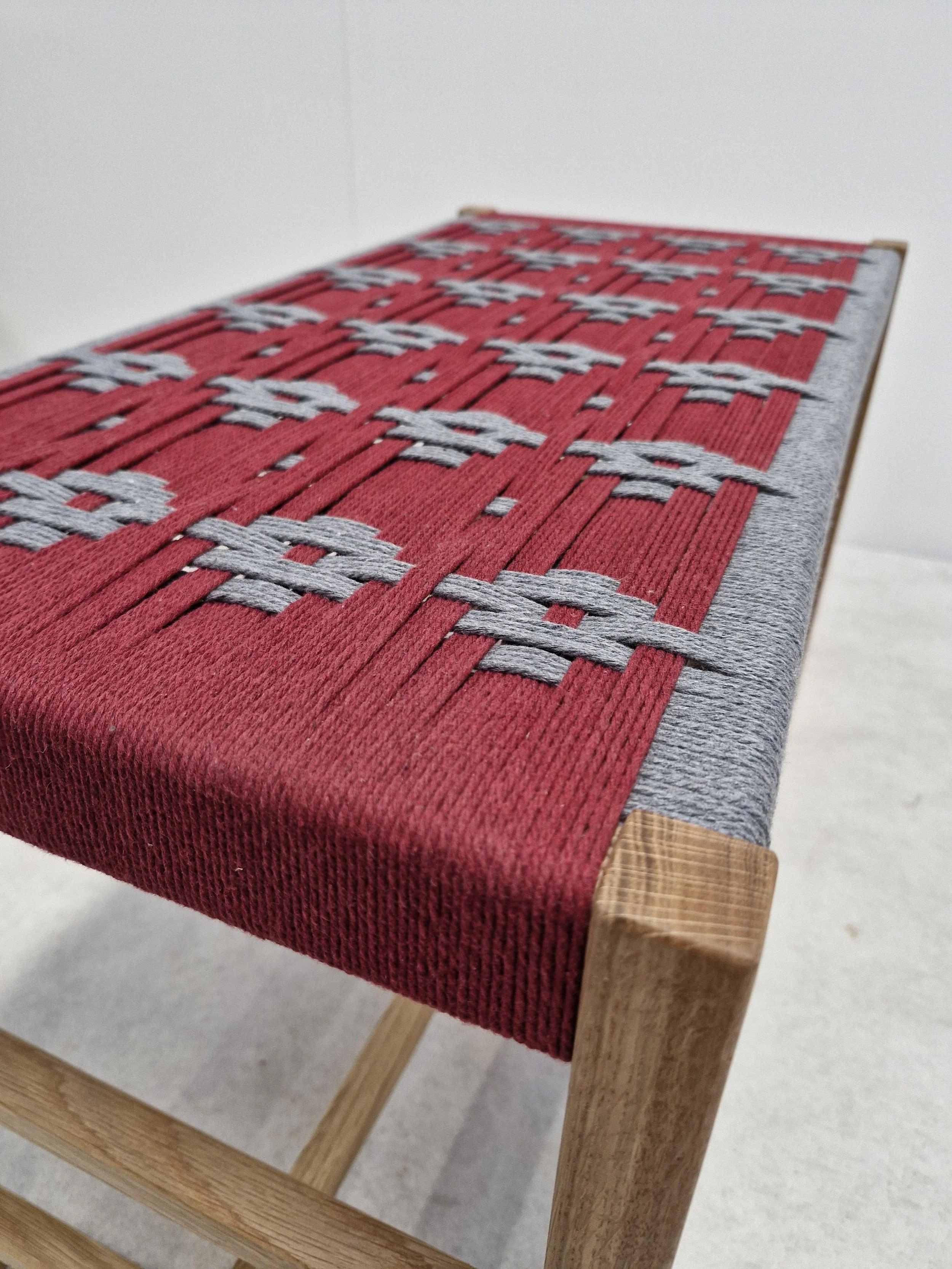 A wooden bench with a woven red and gray fabric seat.