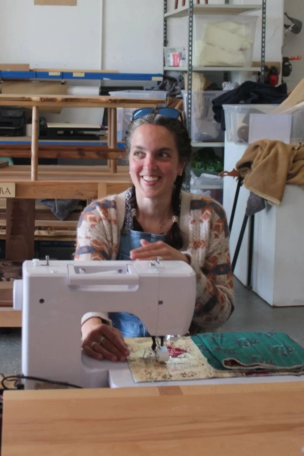 Woman smiling while sewing with a sewing machine at a workshop or studio.