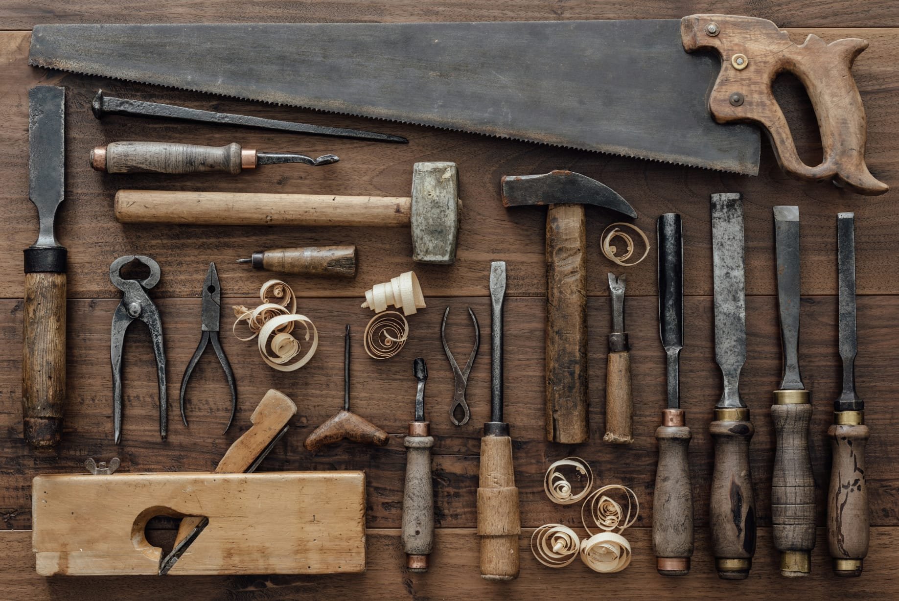 A collection of vintage woodworking tools on a wooden surface, including saws, chisels, planes, and rasps.