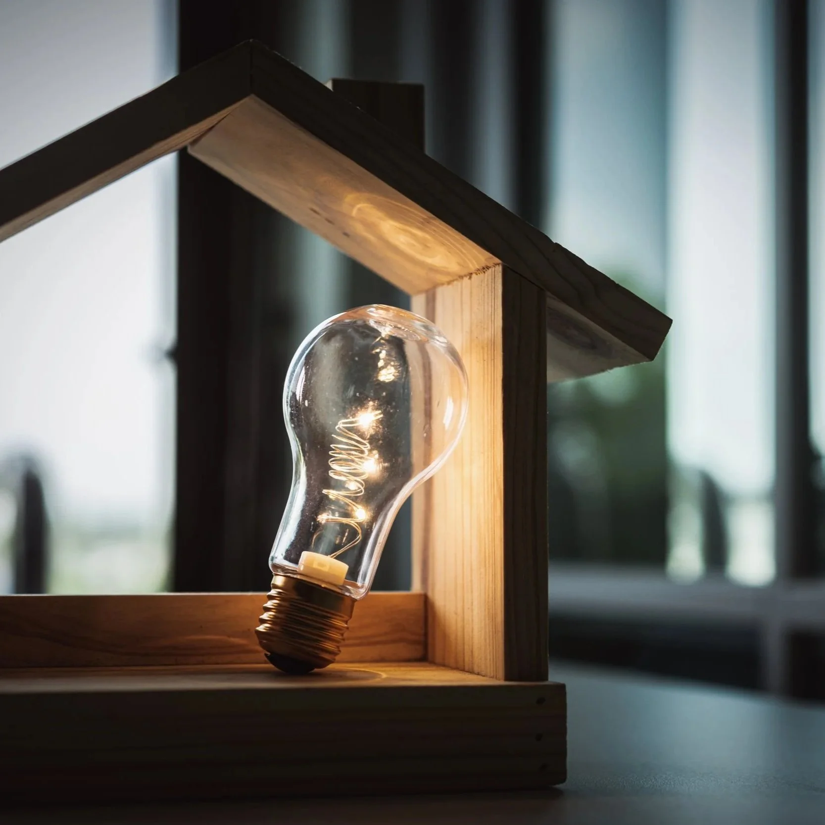 Close-up of a decorative table lamp with a glass bulb, mounted on a wooden frame with a glowing filament inside, in a dimly lit room.