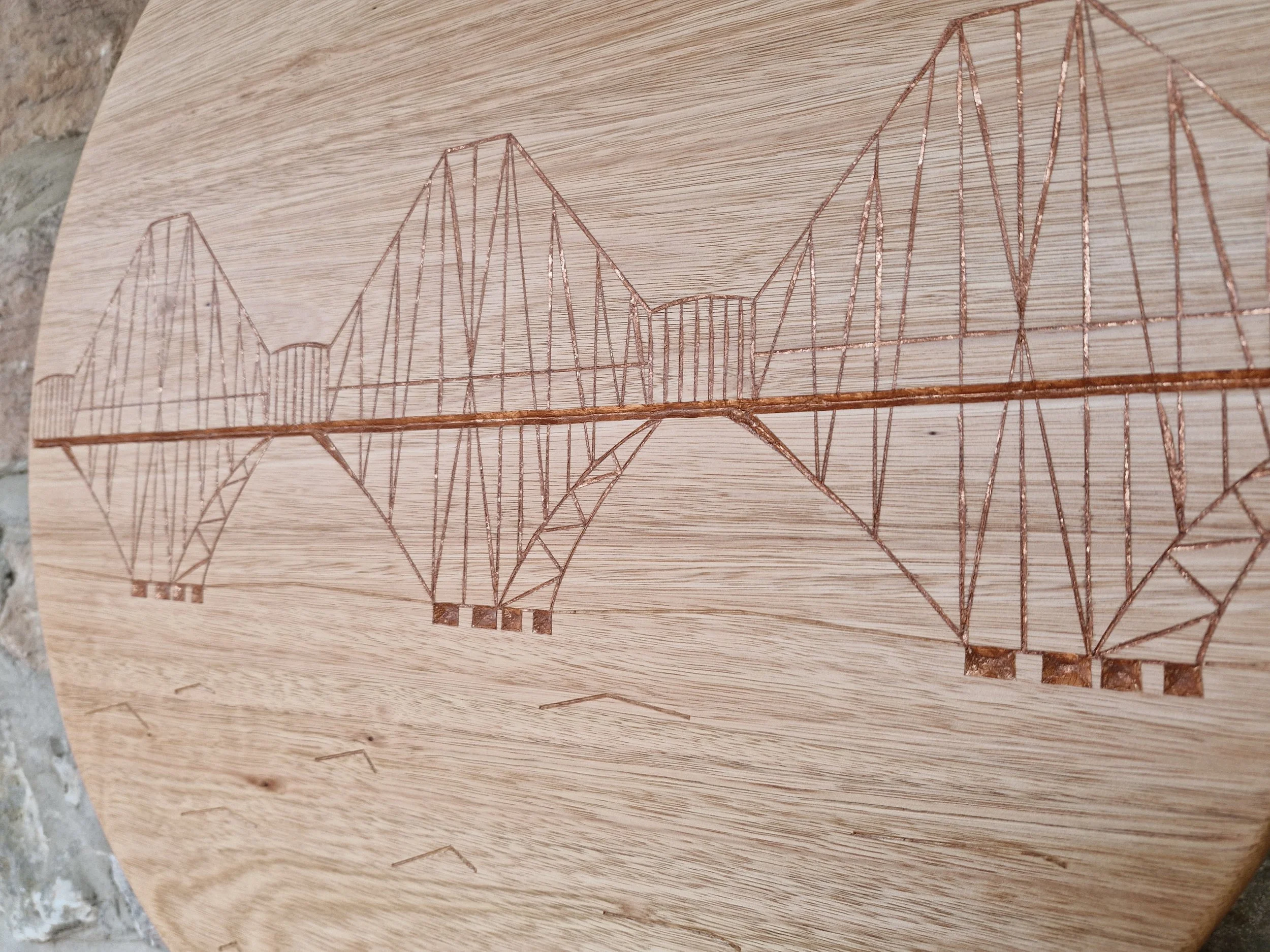 A wooden piece with a detailed engraving of a bridge, possibly a suspension bridge, etched into its surface.