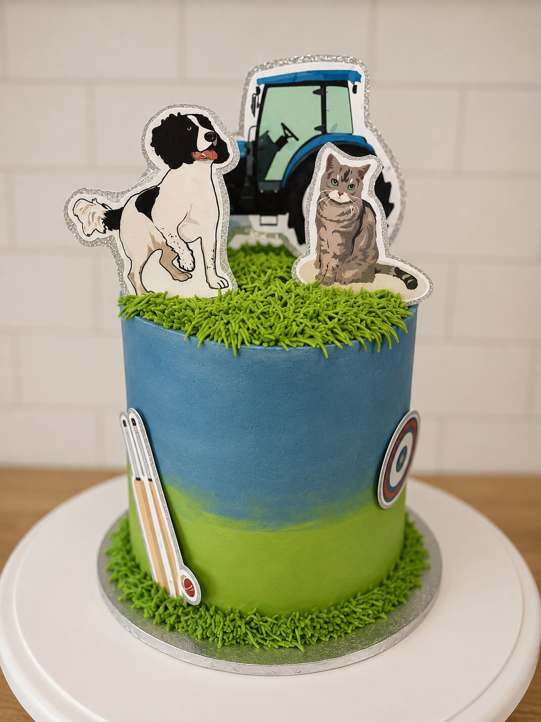 Cake decorated with a farm tractor, a dog, and a cat, featuring green grass and outdoor-themed decorations.