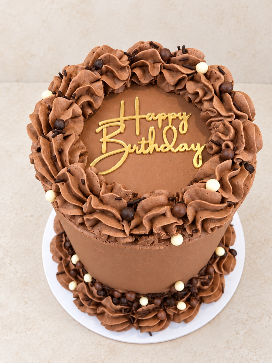 Chocolate bento birthday cake with ruffled frosting border, decorated with round chocolate and white balls, with a yellow "Happy Birthday" message on top.