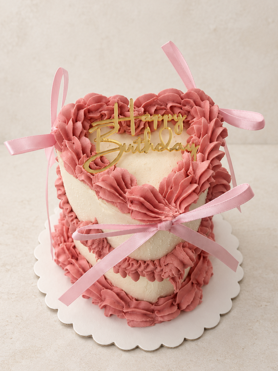 heart bento cake decorated with pink and red buttercream roses and green leaves on top, set on a silver cake board.