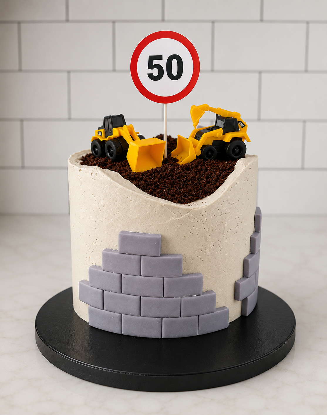 A construction-themed cake decorated with toy construction vehicles, a traffic sign with the number 50, and gray brick fondant accents.