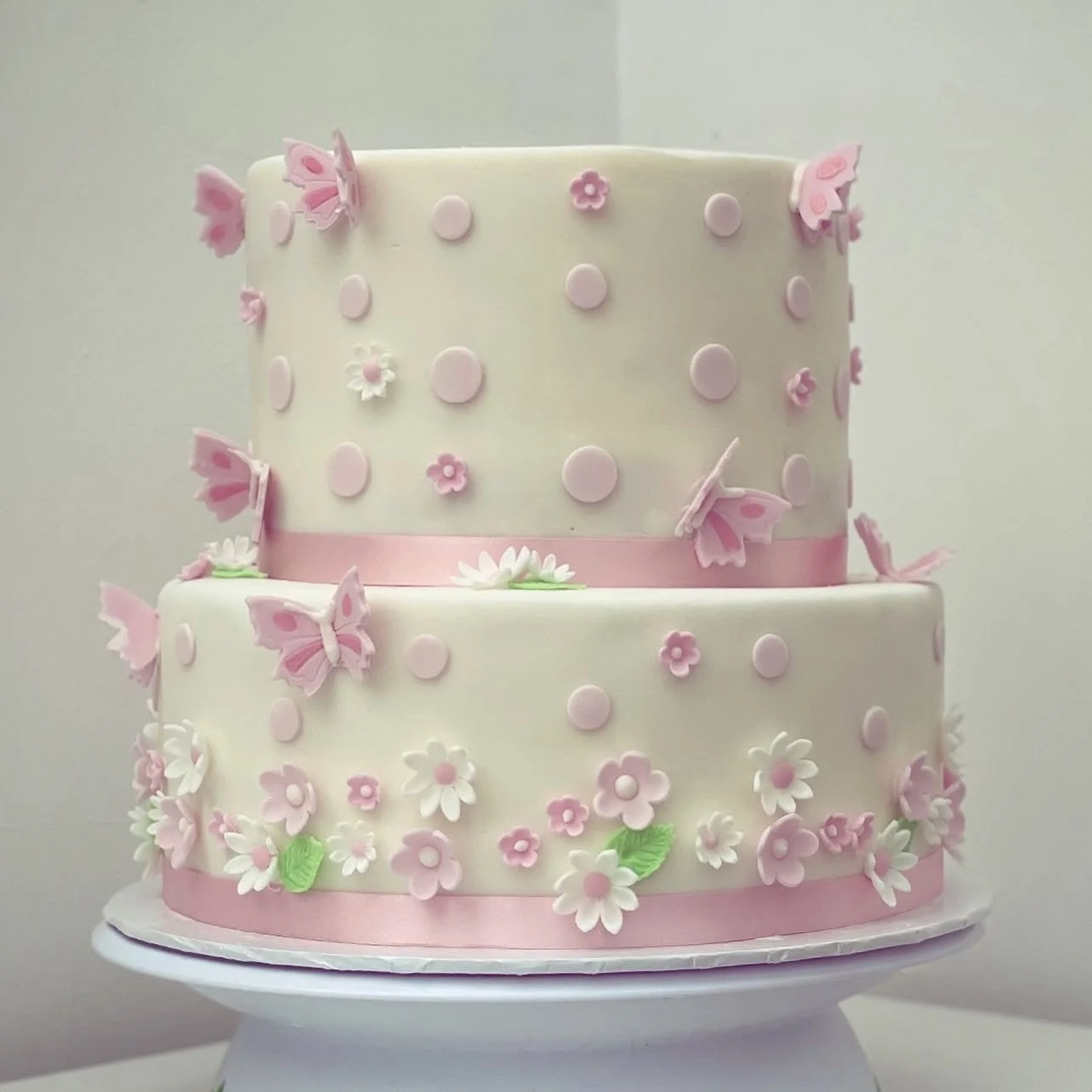 Two-tiered white cake decorated with pink and white flowers and butterflies.