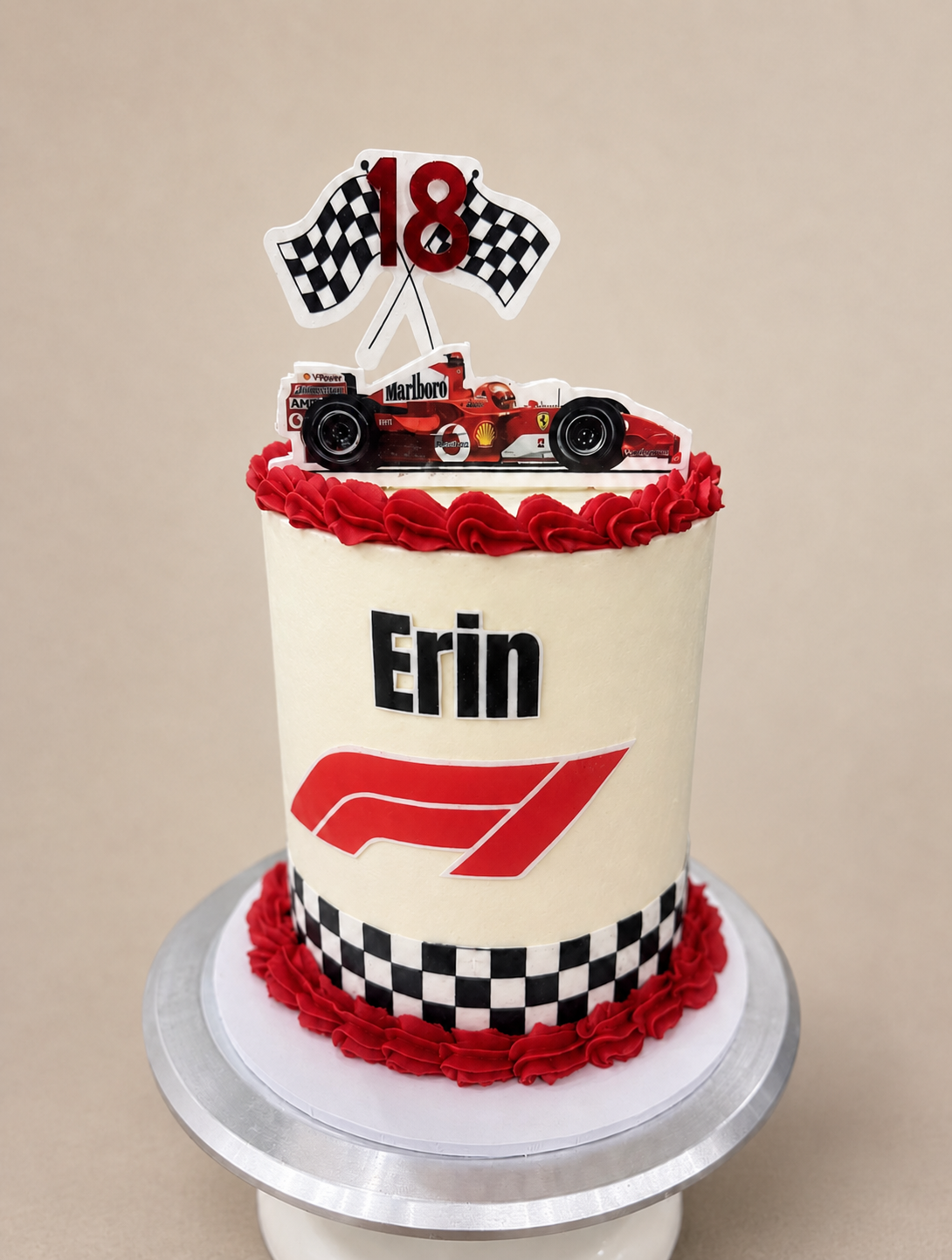 A race car themed birthday cake with a red and white Ferrari F1 car topper, checkered flags, a red number 18, and the name 'Erin' on the front.