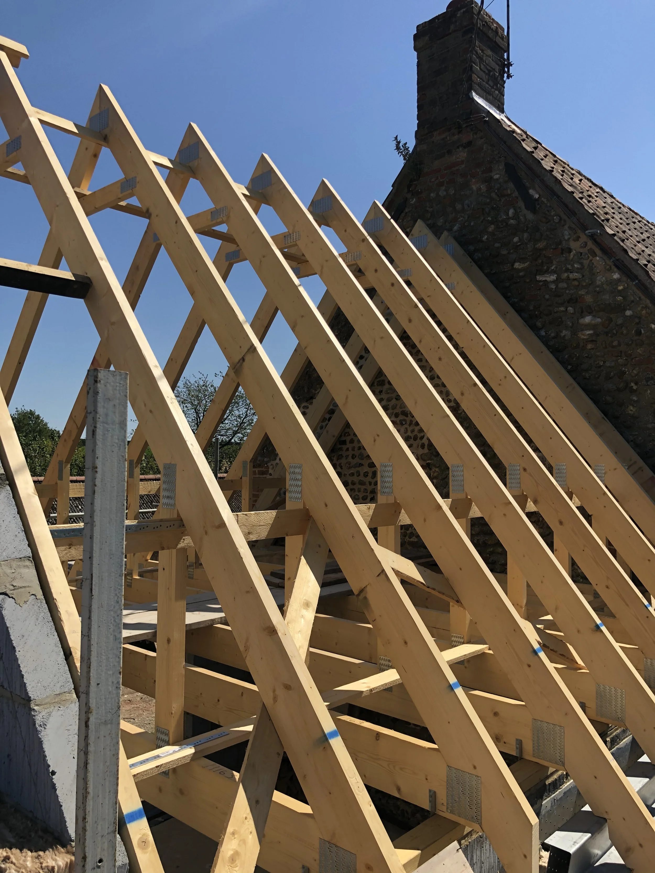 Wooden roof trusses being constructed on a building under a clear blue sky.