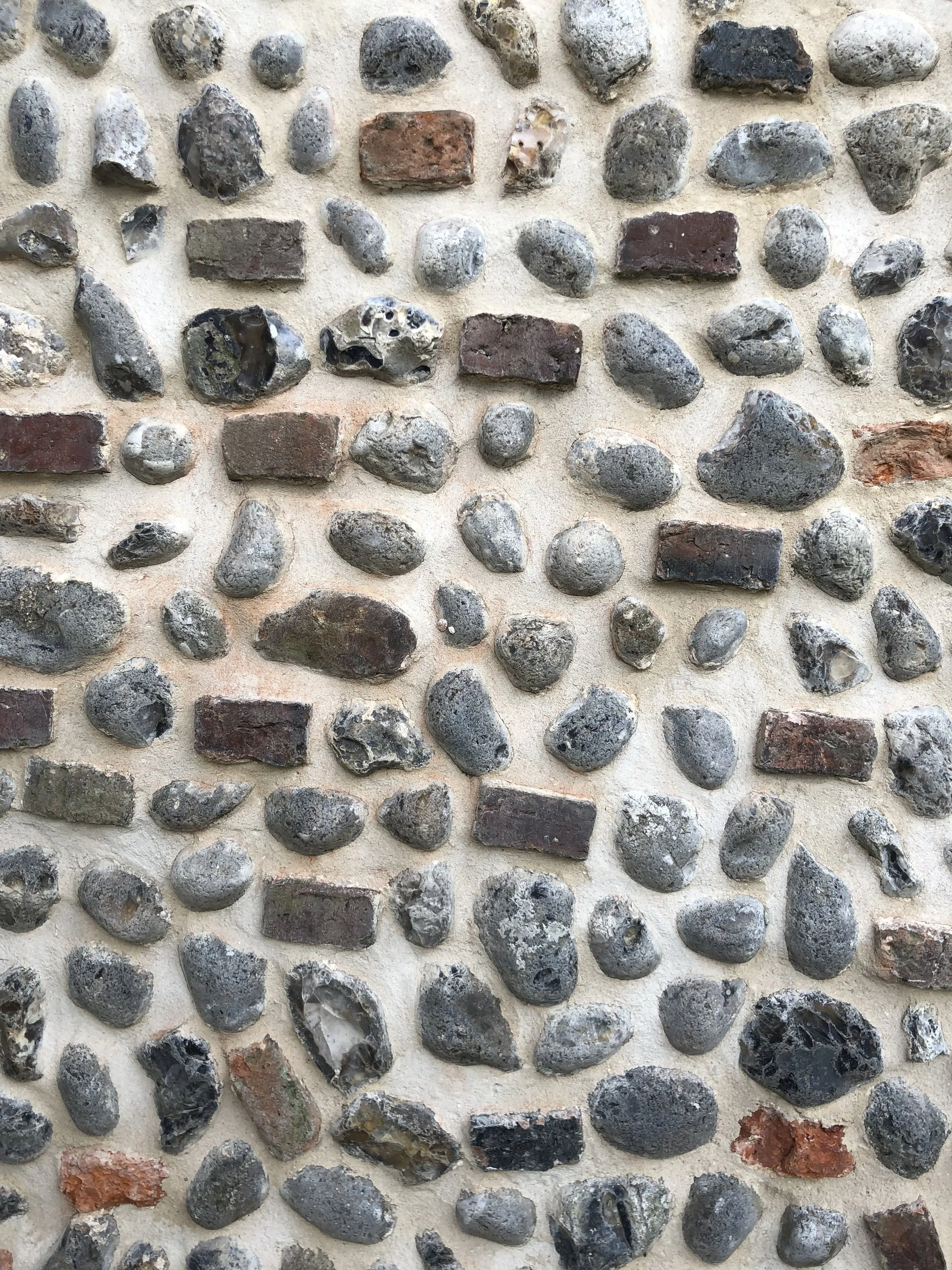 Close-up view of a wall made of various irregularly shaped stones and red bricks set in mortar.