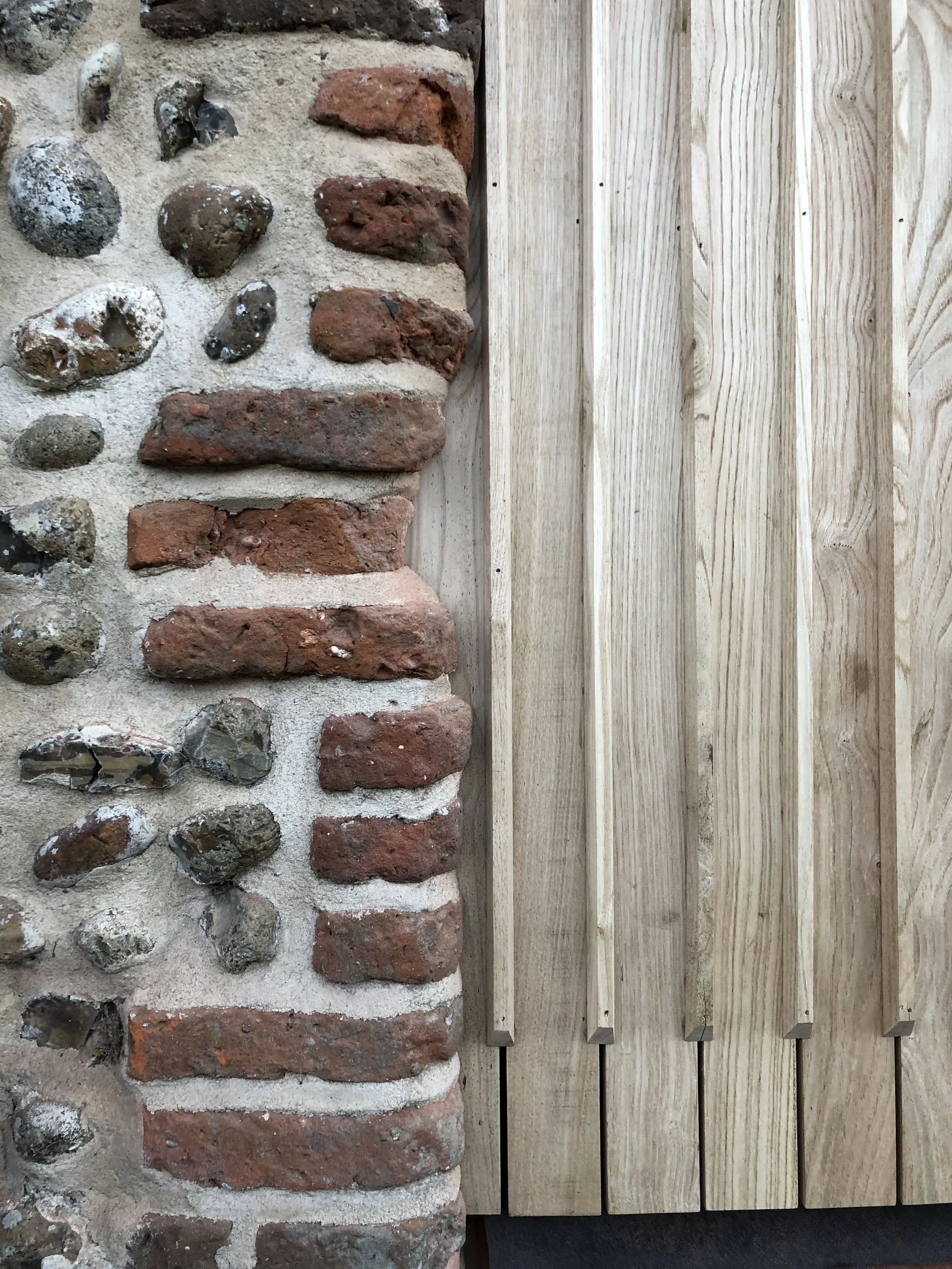 A combination of a brick and stone wall with a wooden slat fence next to it.