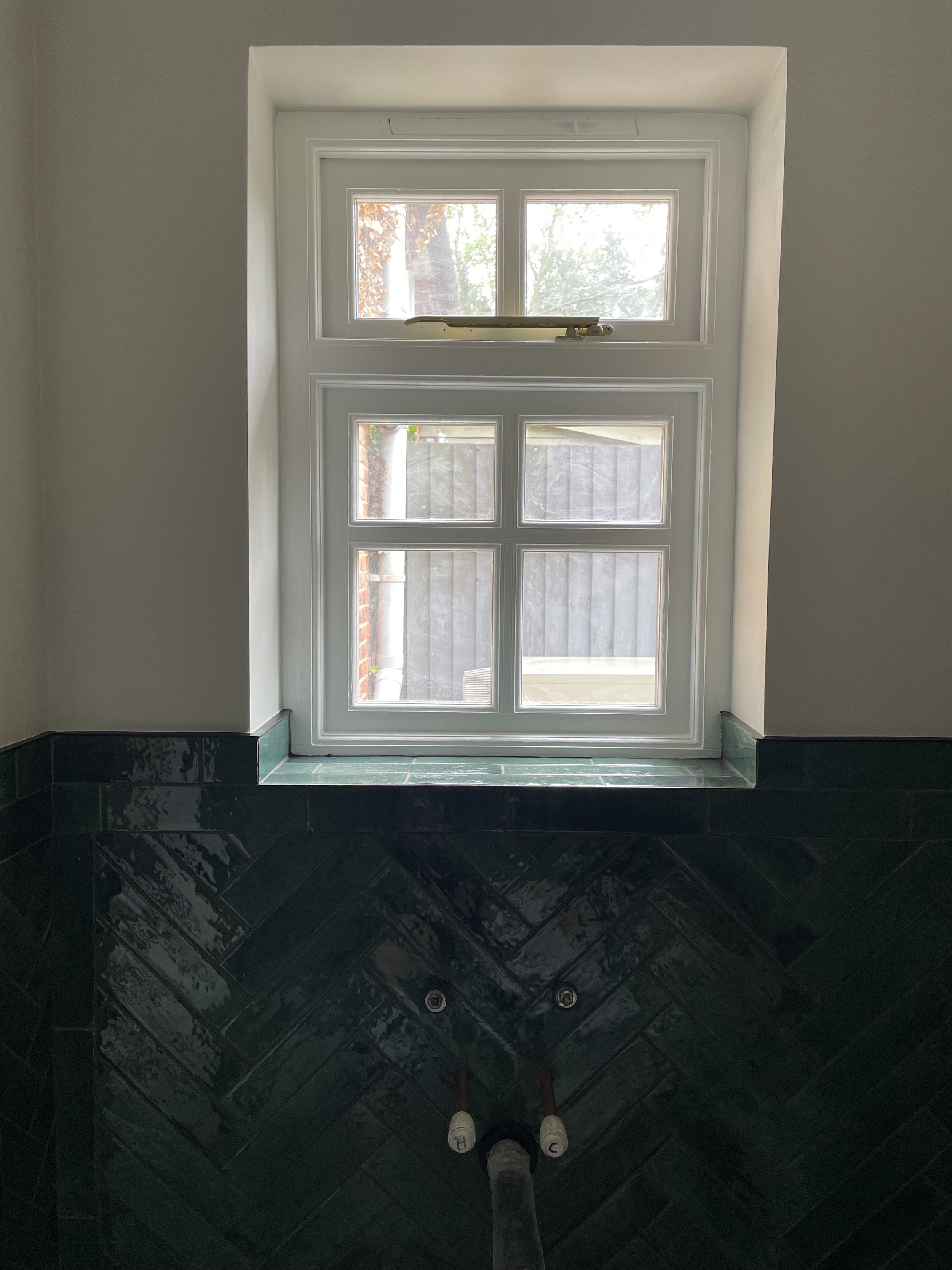 Looking down at a white-framed window and a person wearing white sneakers reflected in a shiny black tiled floor.