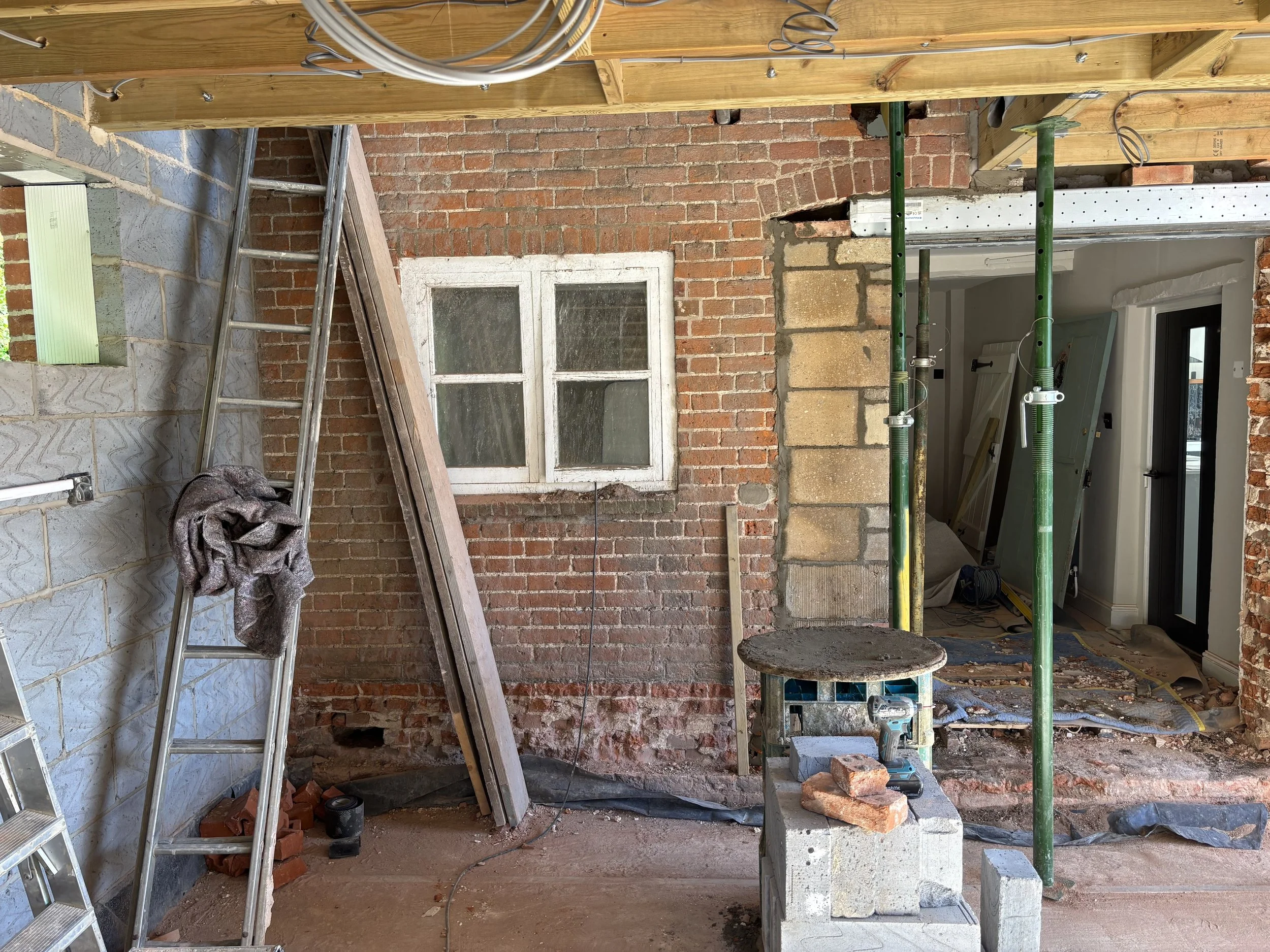 Construction site with scaffolding, brick wall, wooden panels, a ladder, and construction tools.