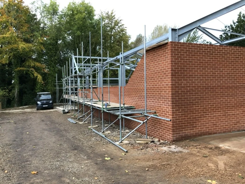 Construction scaffolding around a brick building with trees in the background.