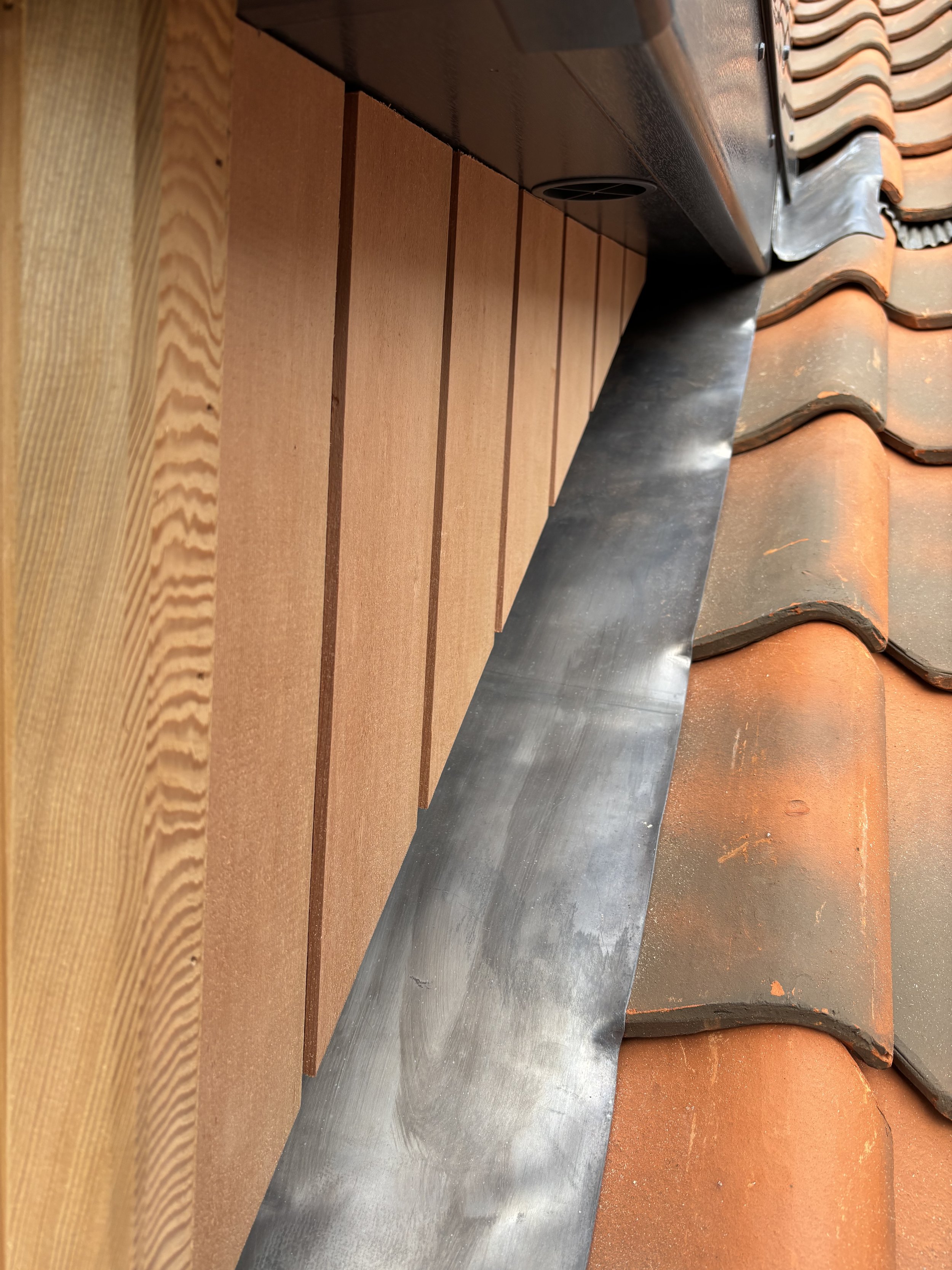 Close-up view of wooden wall panels, metal flashing, and roof tiles seen from below.