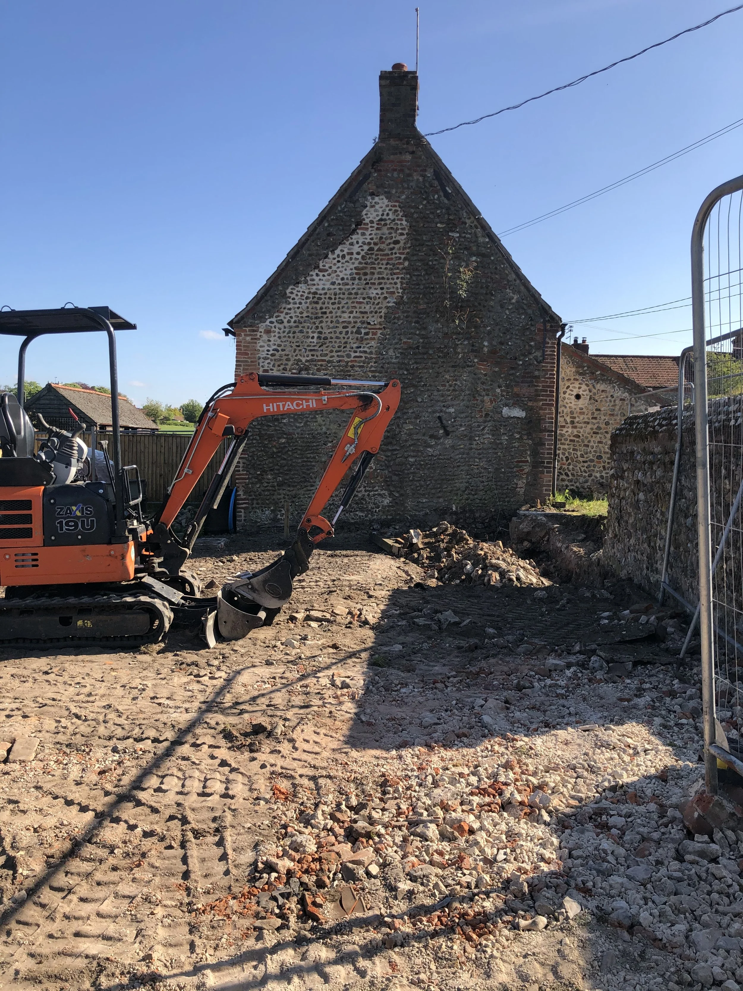 A construction site with a small orange excavator and a pile of rubble in front of an old stone and brick building during daytime.
