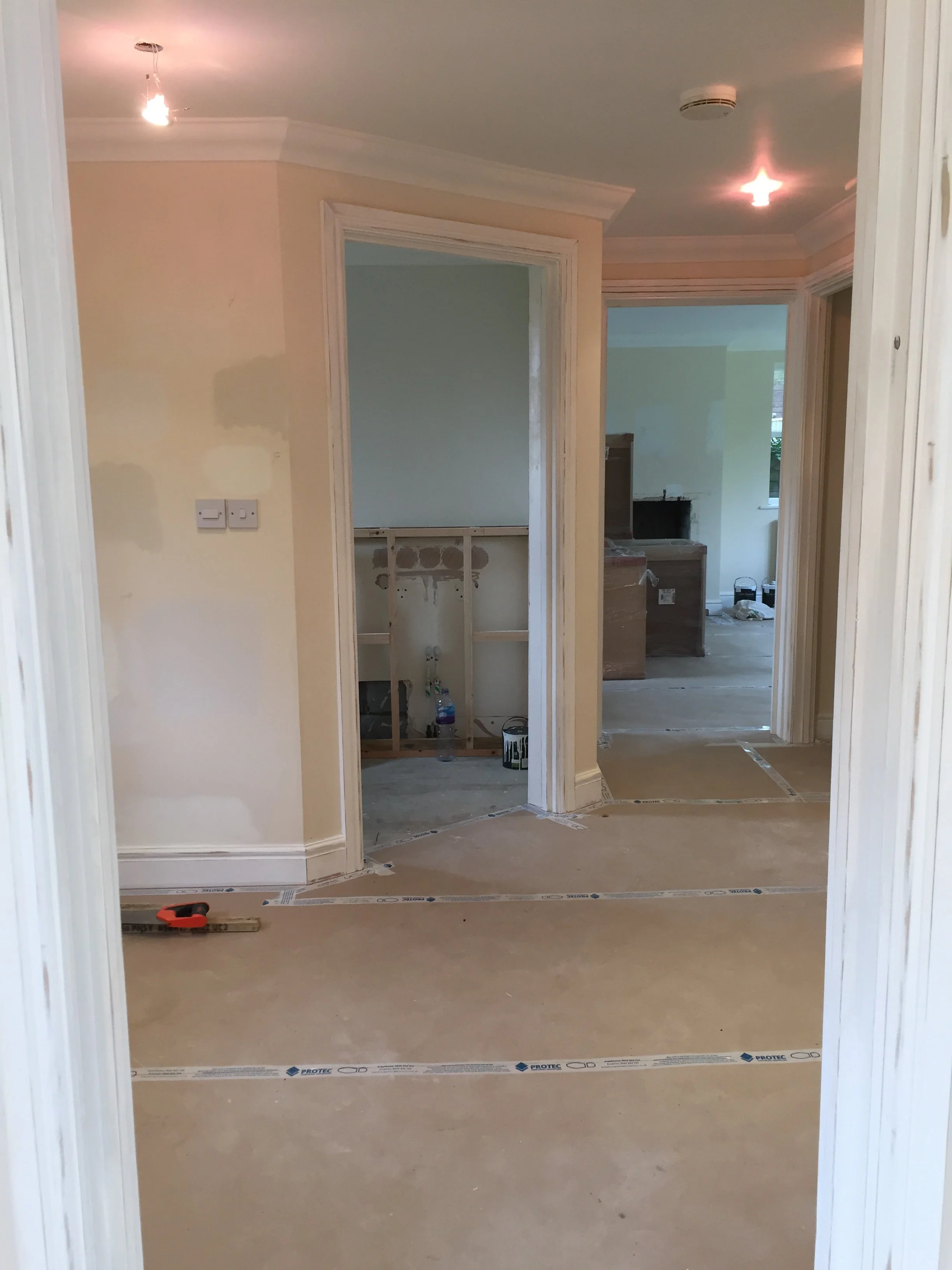 Interior view of a home under renovation, showing open doorways, construction materials, and partially finished rooms with unpainted walls and flooring.