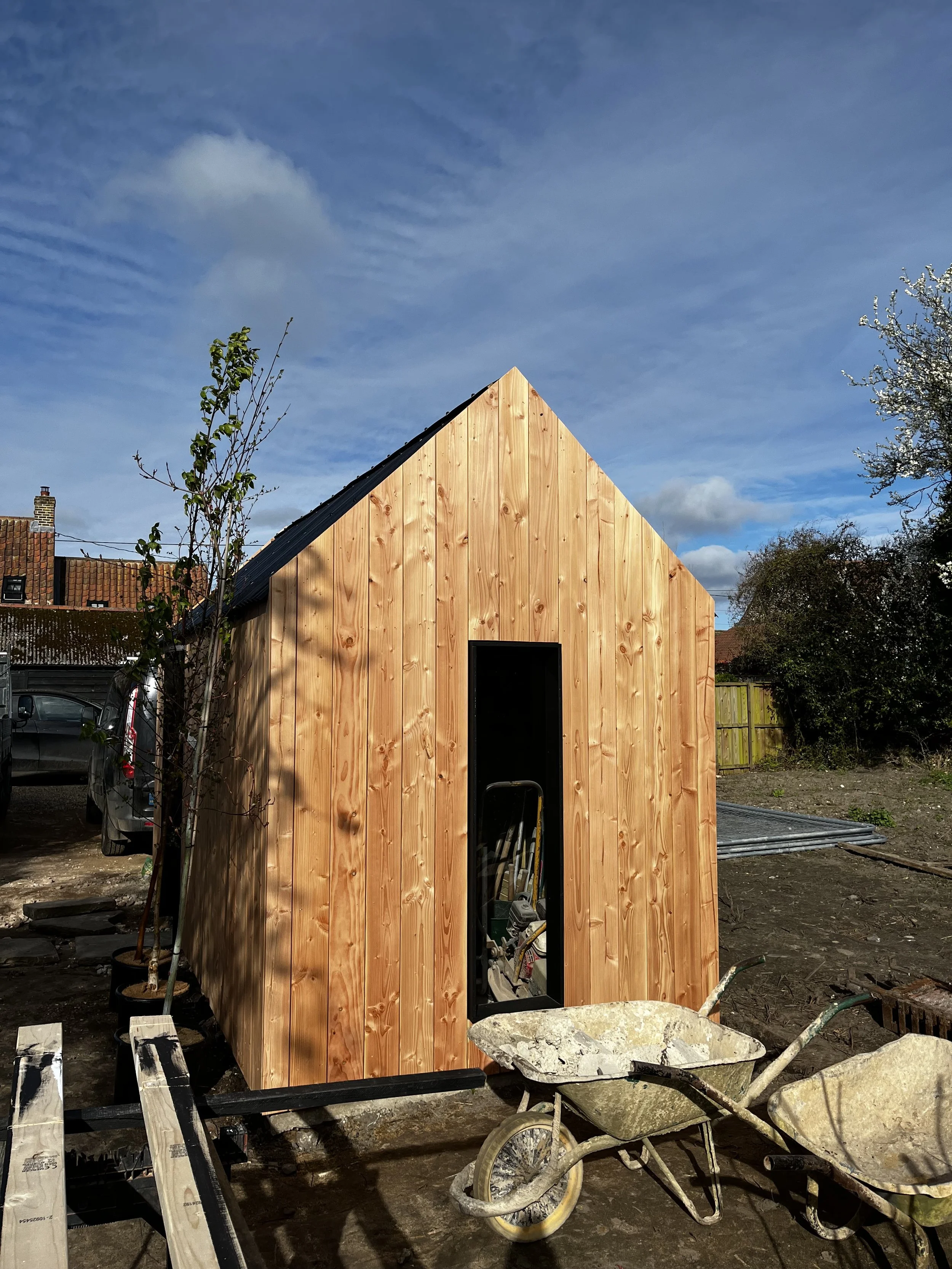 A small building under construction with wooden siding and a door opening, surrounded by construction tools and materials outside.