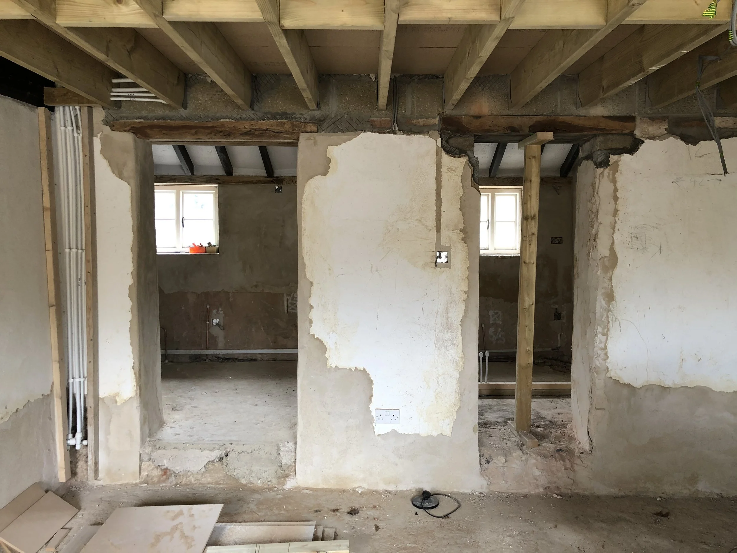 Interior of a house under renovation with exposed wooden beams, partially torn drywall, and construction wiring.