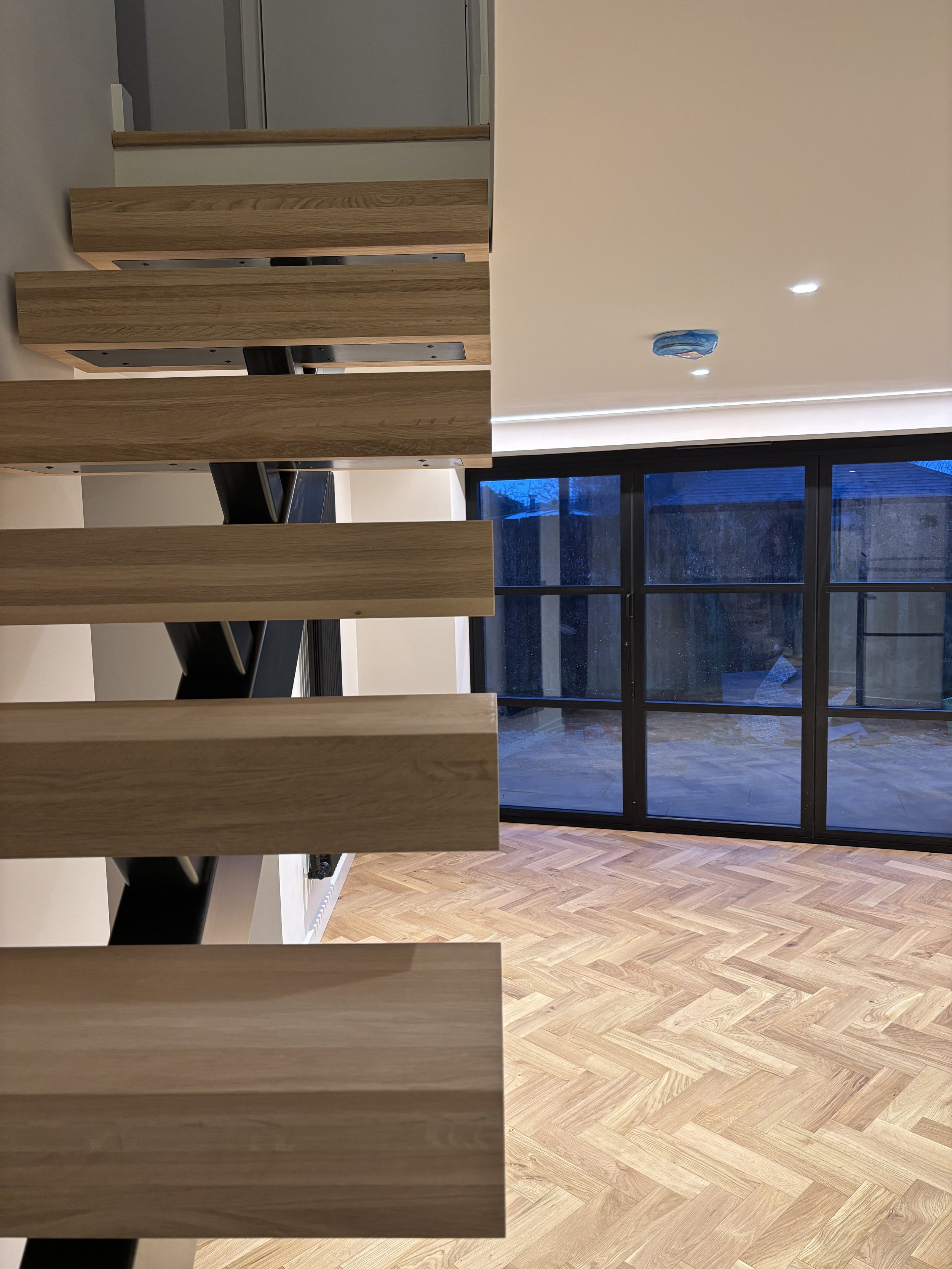 Wooden staircase railing viewed from below with a glass window and wooden floor visible in the background.