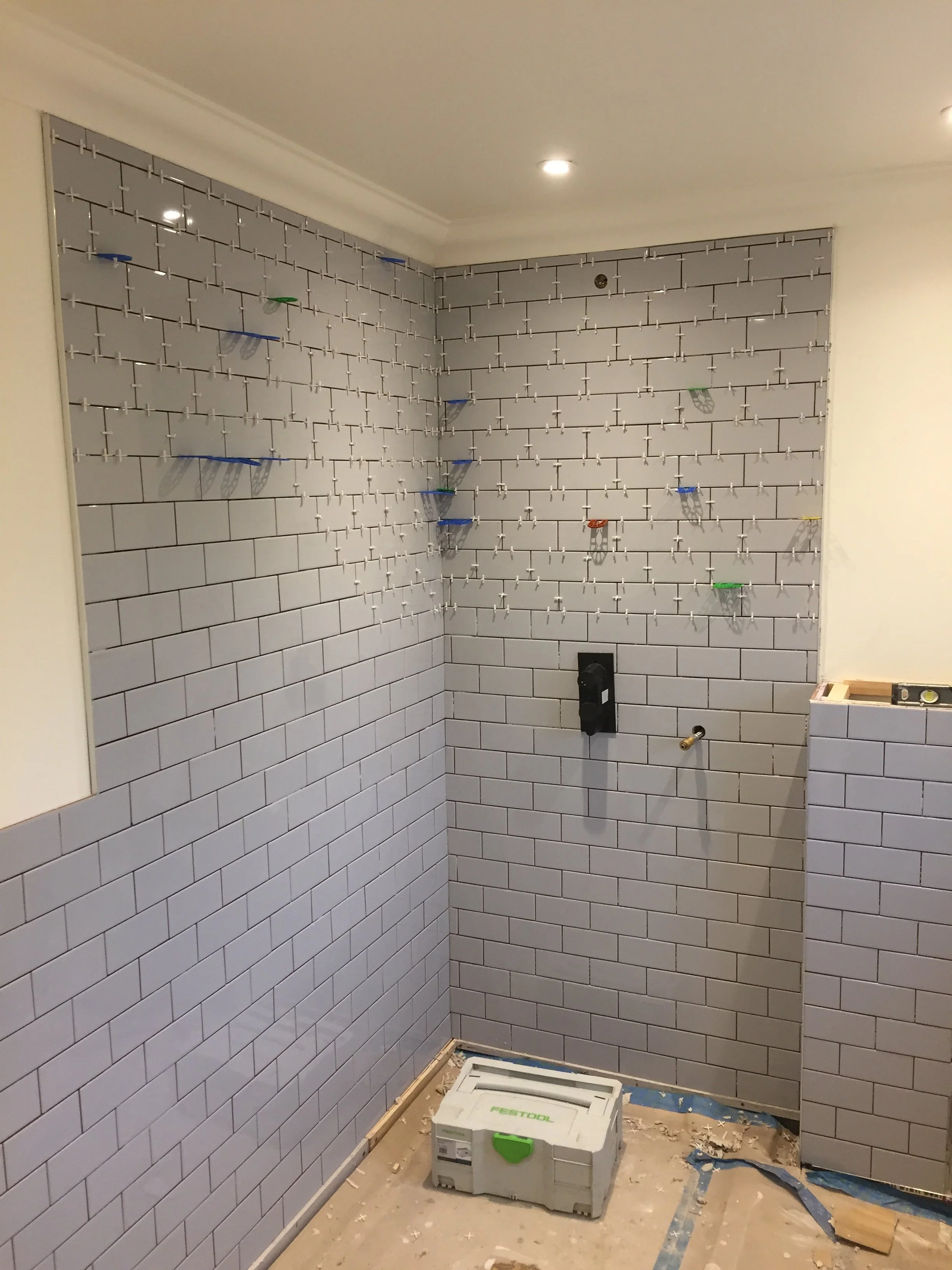 Bathroom under renovation with tiled walls, construction tools, and a toolbox on the floor.