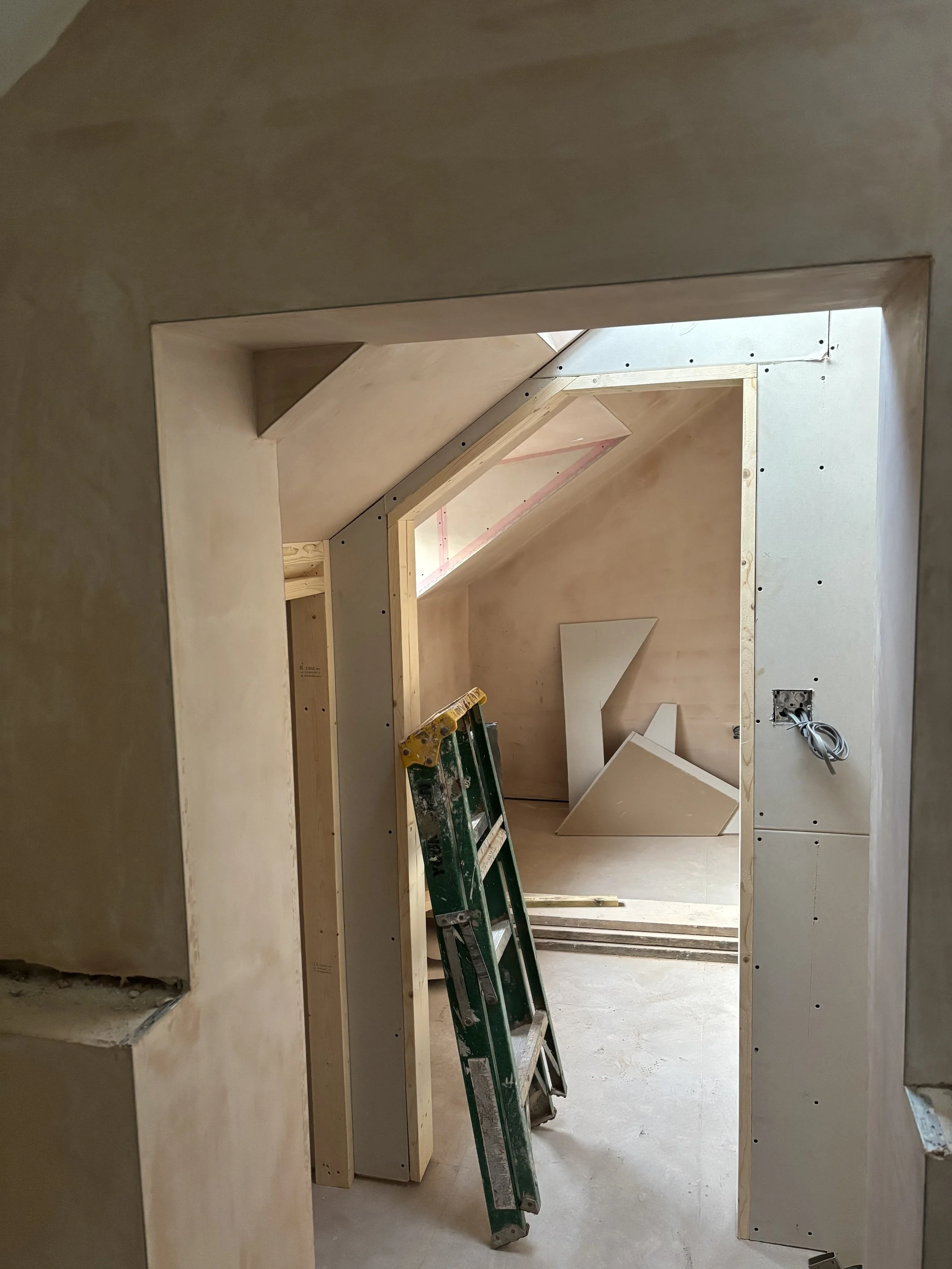 Interior of a building under construction, showing unfinished walls, a ladder, and construction materials.