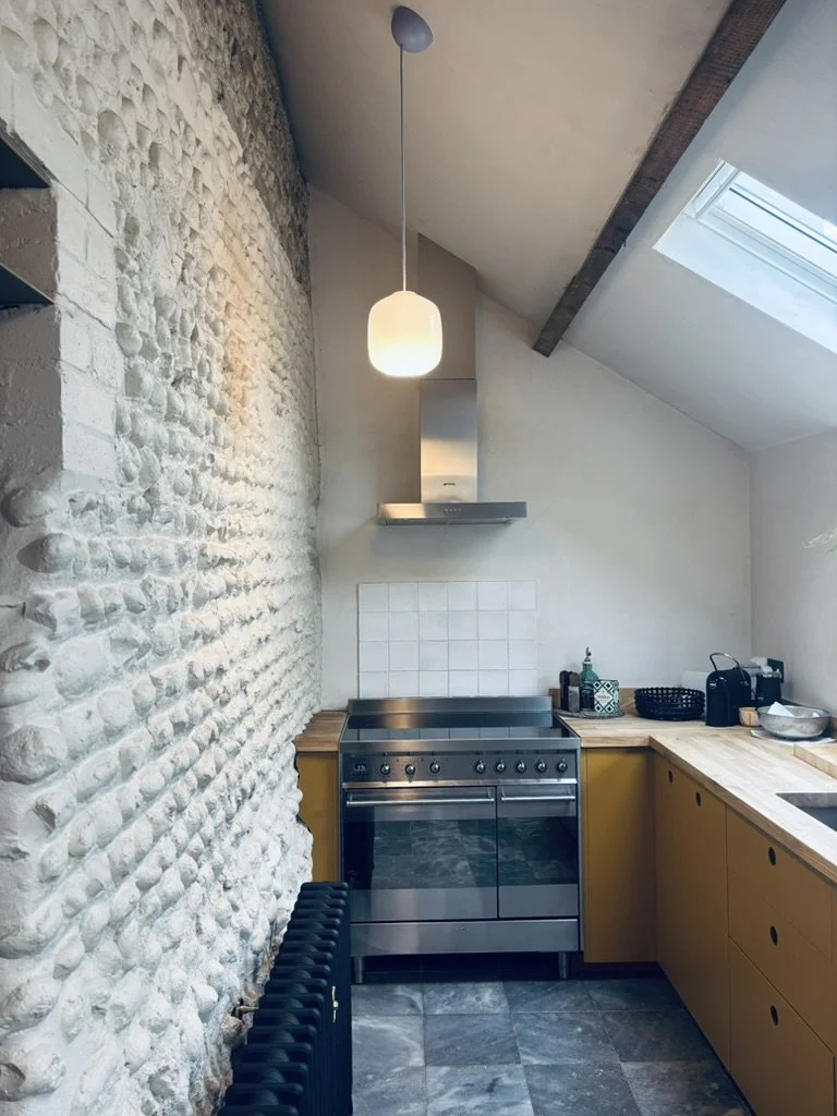 A modern kitchen with a stone wall on the left, wooden cabinets on the right, a stainless steel stove, white tile backsplash, and a skylight in the sloped ceiling.