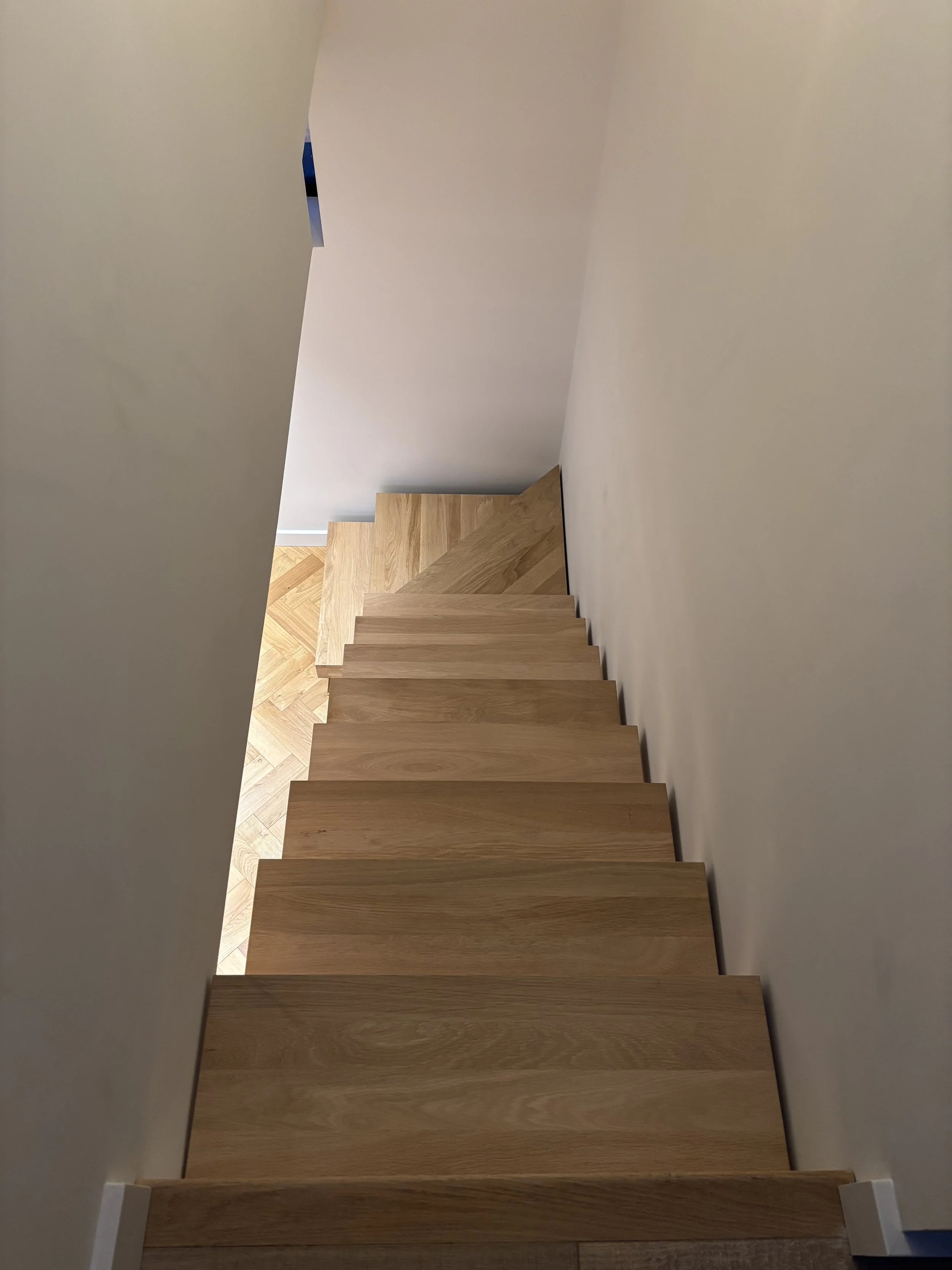 Wooden staircase descending along a white wall in a modern interior.