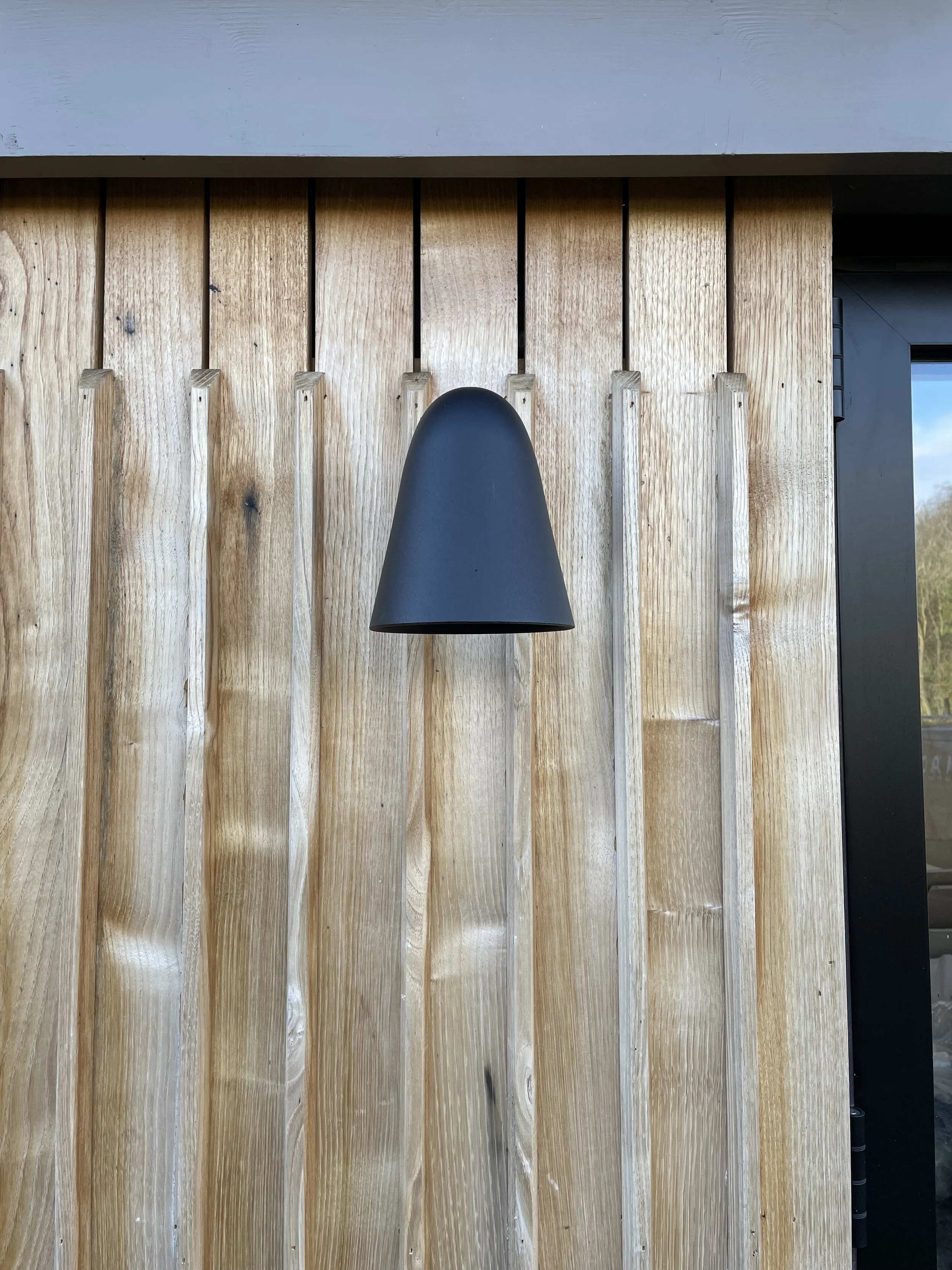 A black pendant light hanging in front of a natural wood plank wall inside a building.