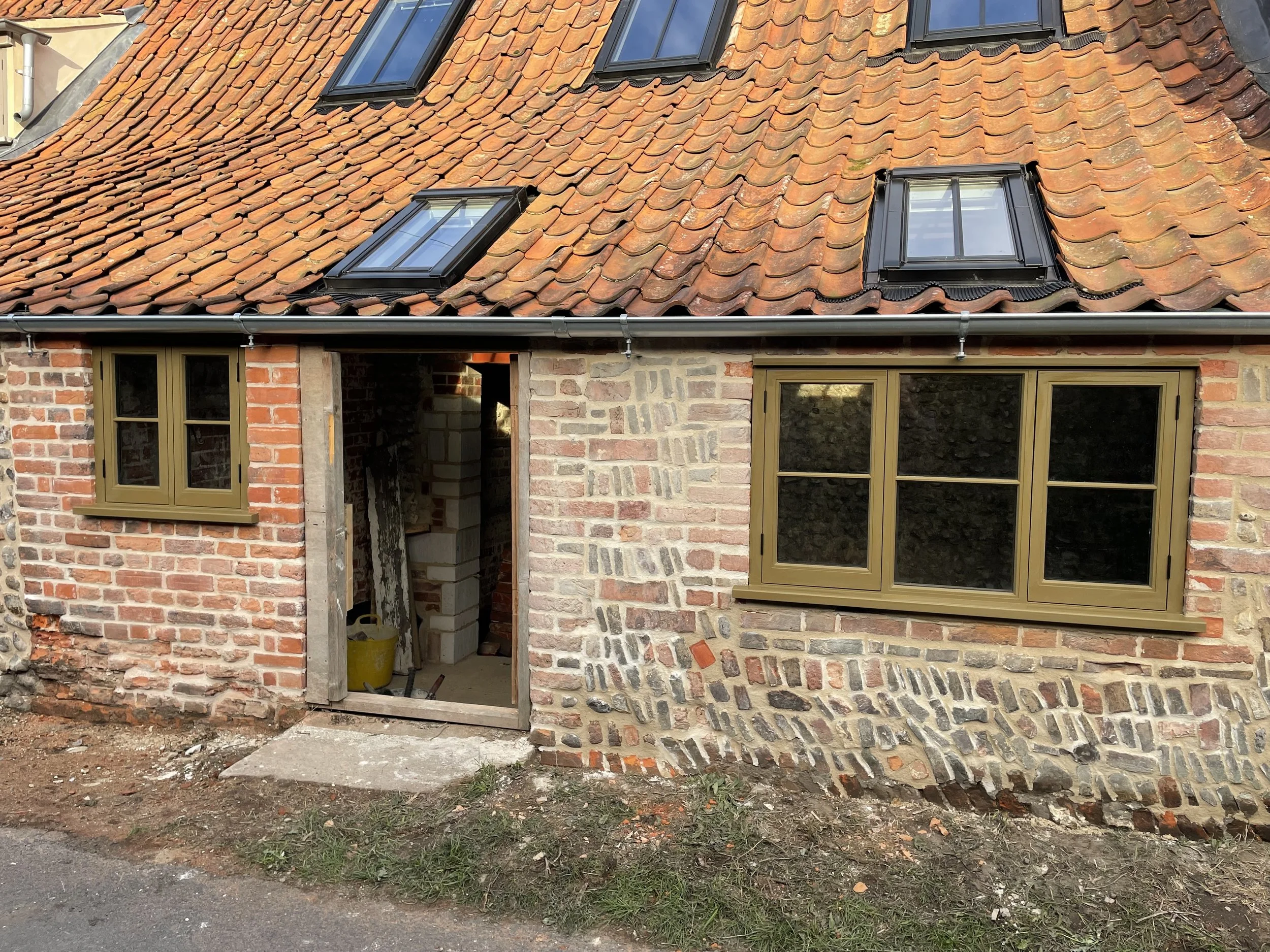 View of a house roof with orange clay tiles and black skylights, and a brick wall below with a partially open door under construction.