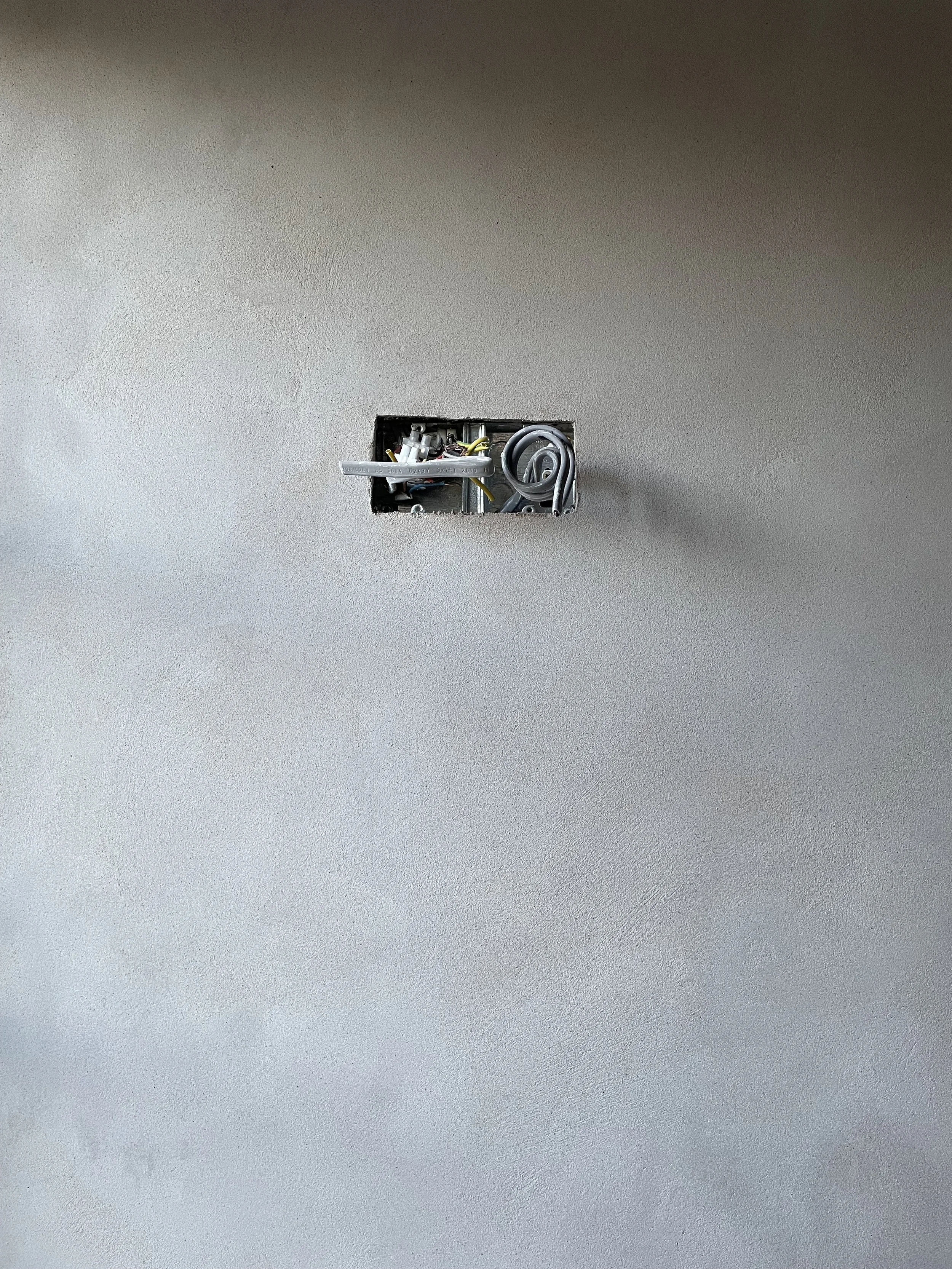 Close-up of an electrical outlet box in a wall with wires and connections visible, without an outlet cover.