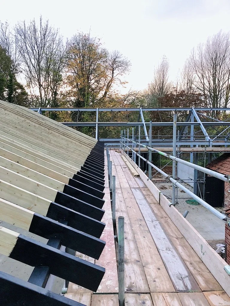 Construction scaffolding and partially built roof with wooden framework on a building, surrounded by trees with bare branches.
