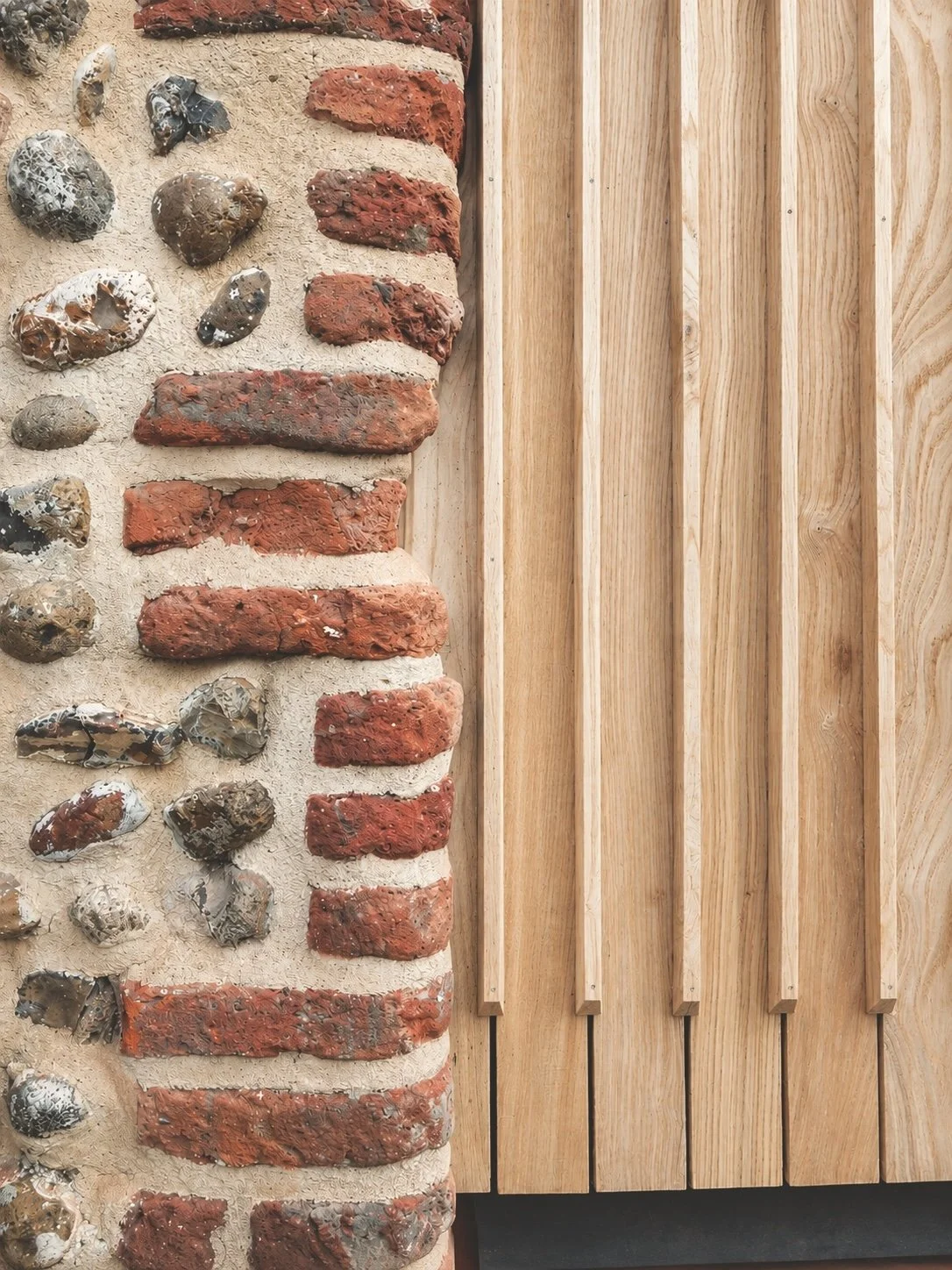 A wall with a combination of exposed red bricks and smooth round stones, partially covered by a wooden panel with vertical slats.