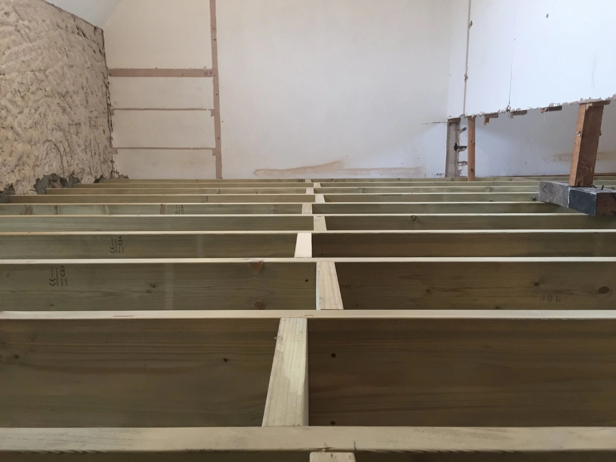 Interior of a room under construction with wooden framing, drywall, and exposed insulation on one side.