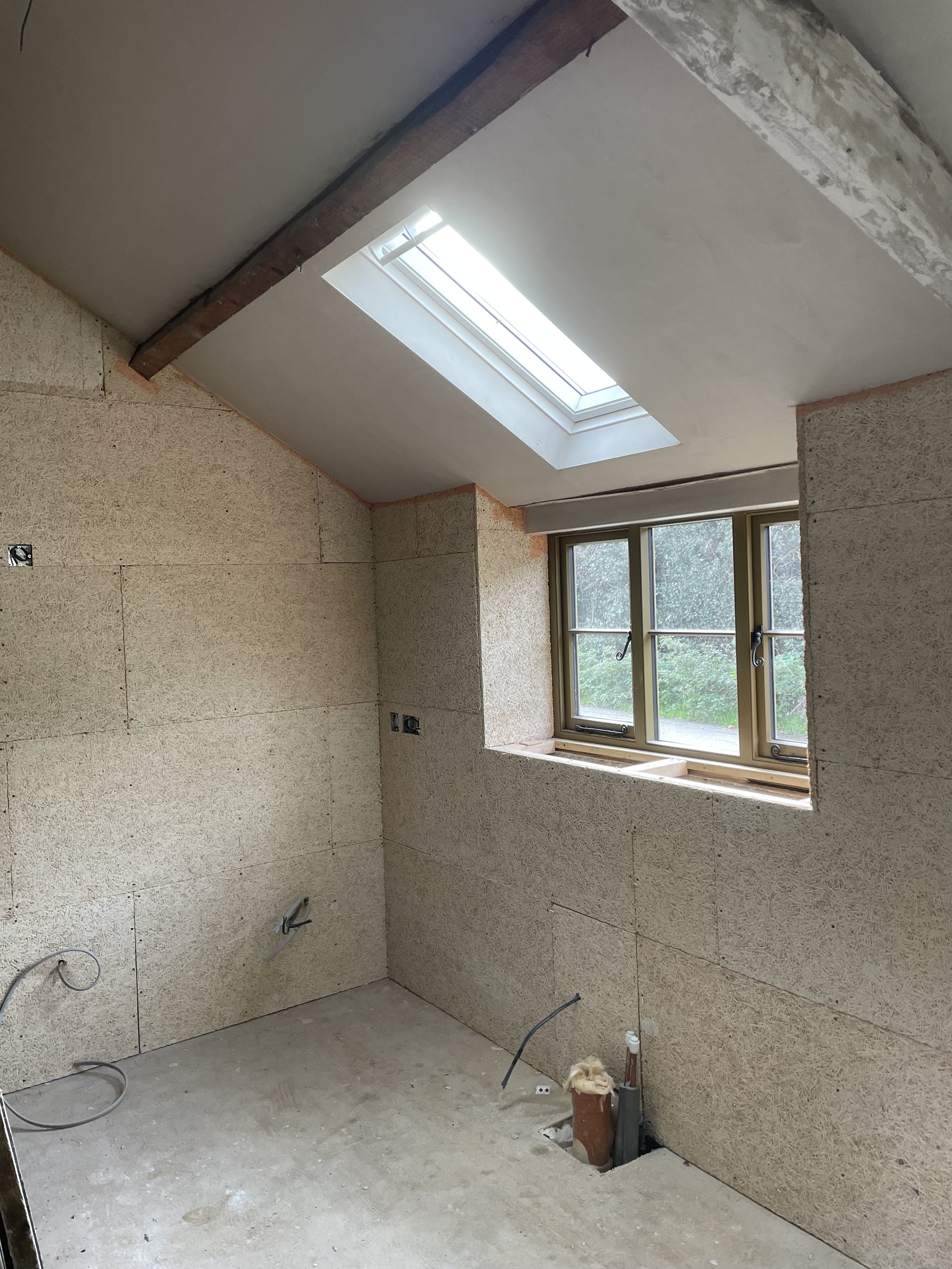 Room under construction with unfinished walls, a window, electrical wires, and fixtures in the process of being installed.