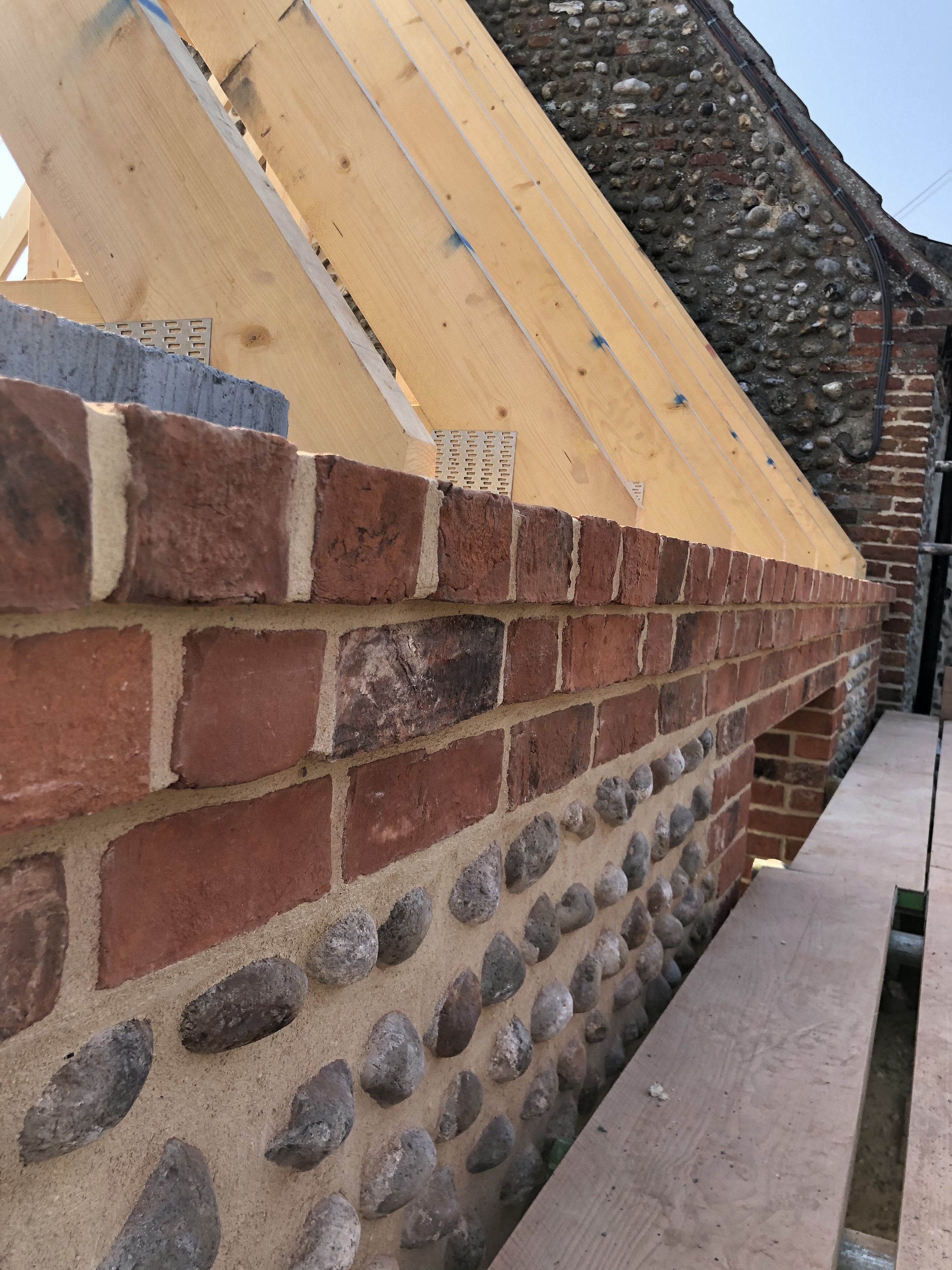 Close-up view of a construction site showing a brick and stone wall with wooden planks and a temporary wooden walkway or platform.
